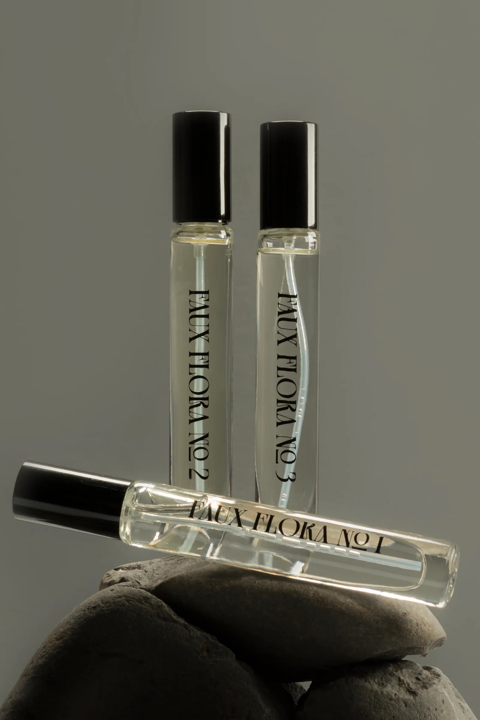 Three small perfume bottles with black caps held by rocks against a gray background ©Fischersund
