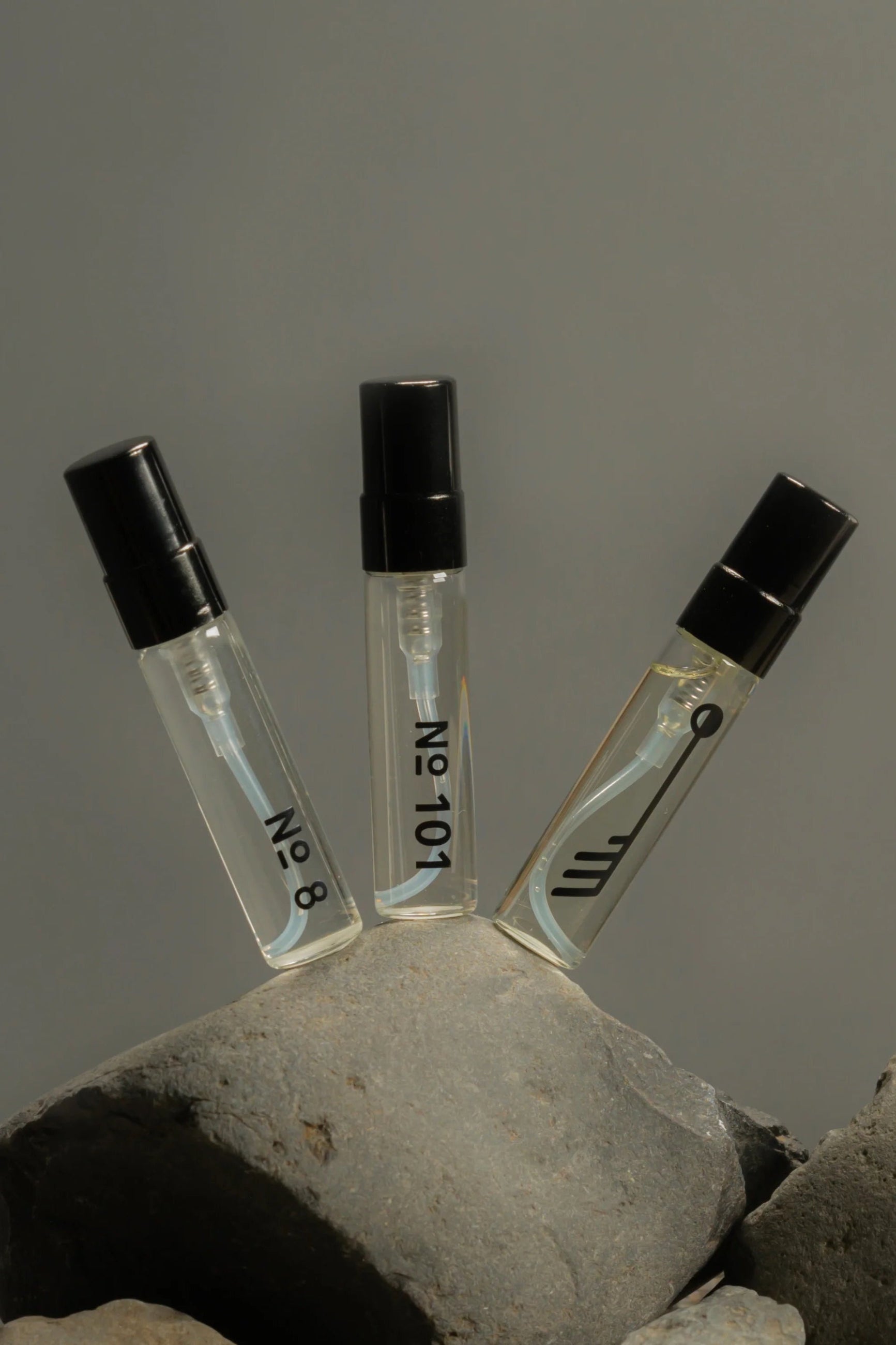 Three small transparent bottles with black caps of the Langdegi (LIGHT) Discover Set on a gray rock against a gray background ©Fischersun