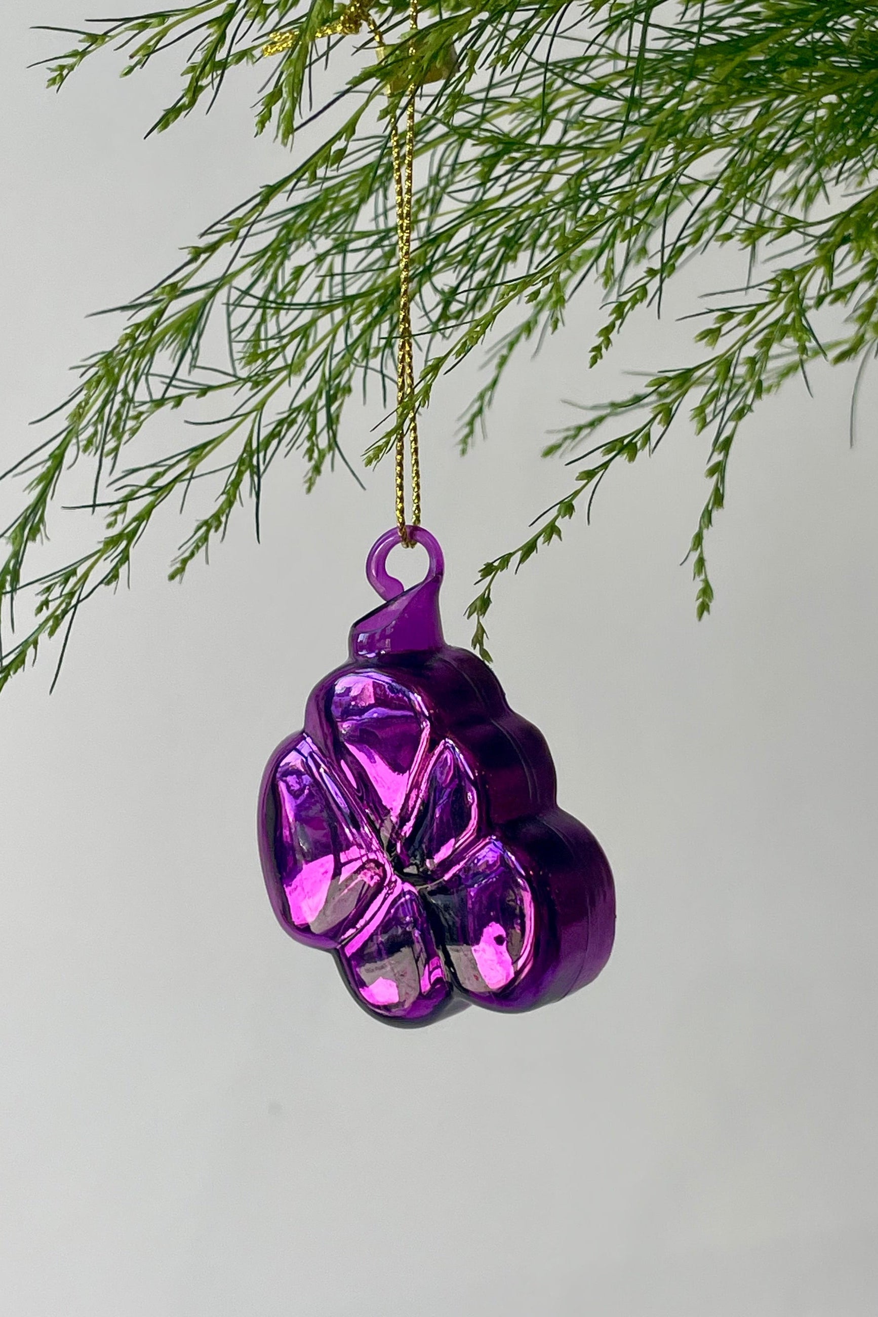 A purple floral ornament shaped like a violet with glitter hangs from a branch in front of a gray wall ©Sprout Home