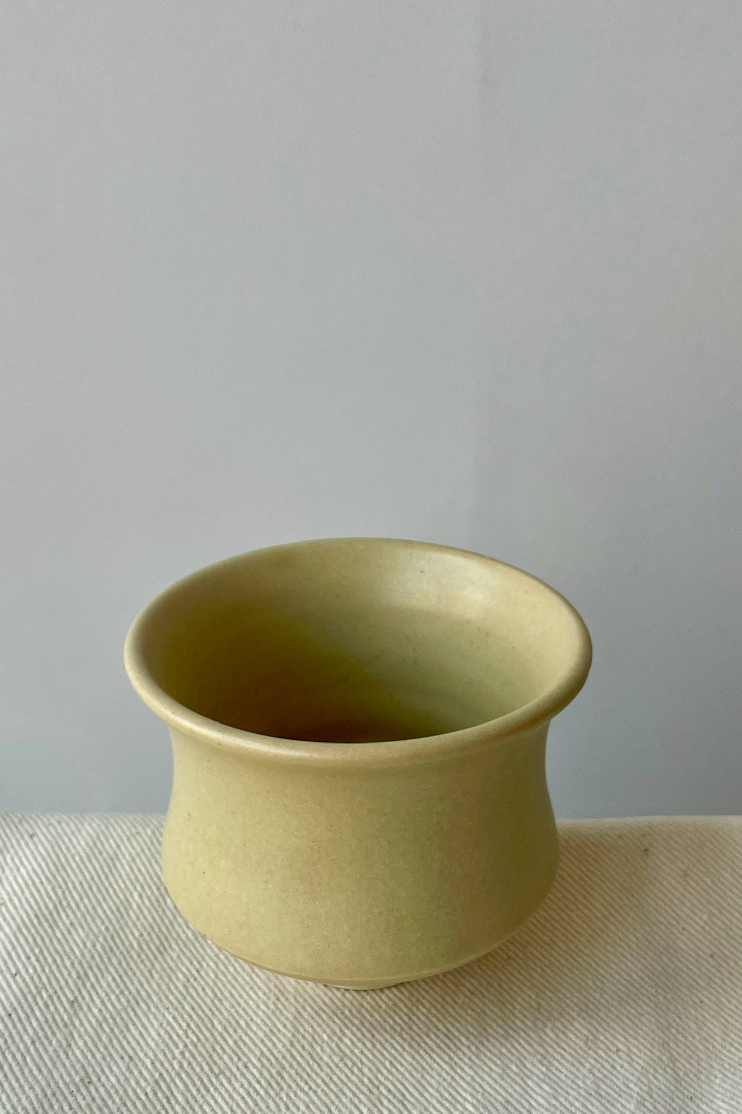 Photo of Little Fire Ceramics hourglass cup with butter glaze shown from the above. The cup sits on a white cloth against a white wall.