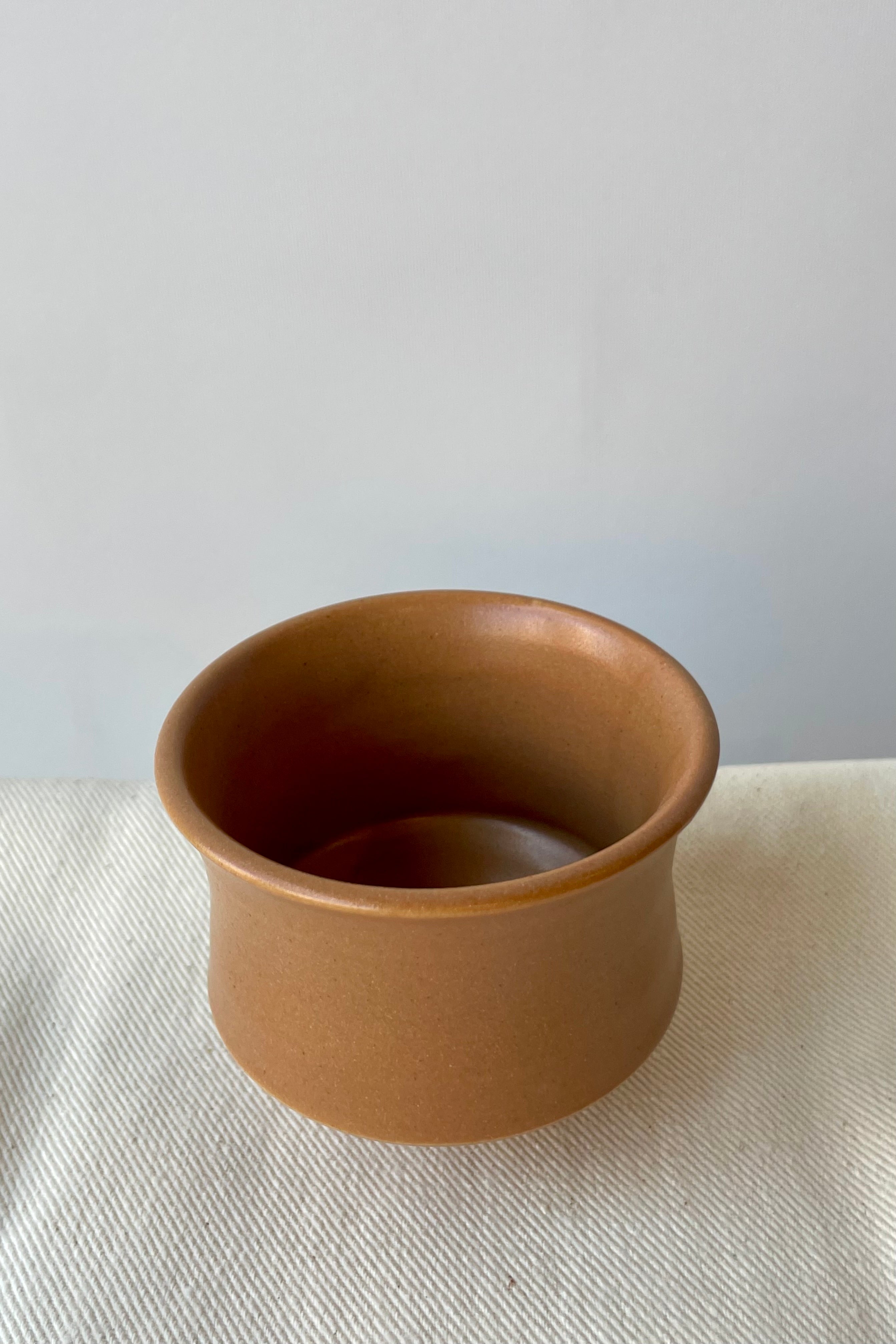 Photo of Little Fire Ceramics Hourglass cup with a camel glaze on a white surface ahead of a white wall. Photo from above.