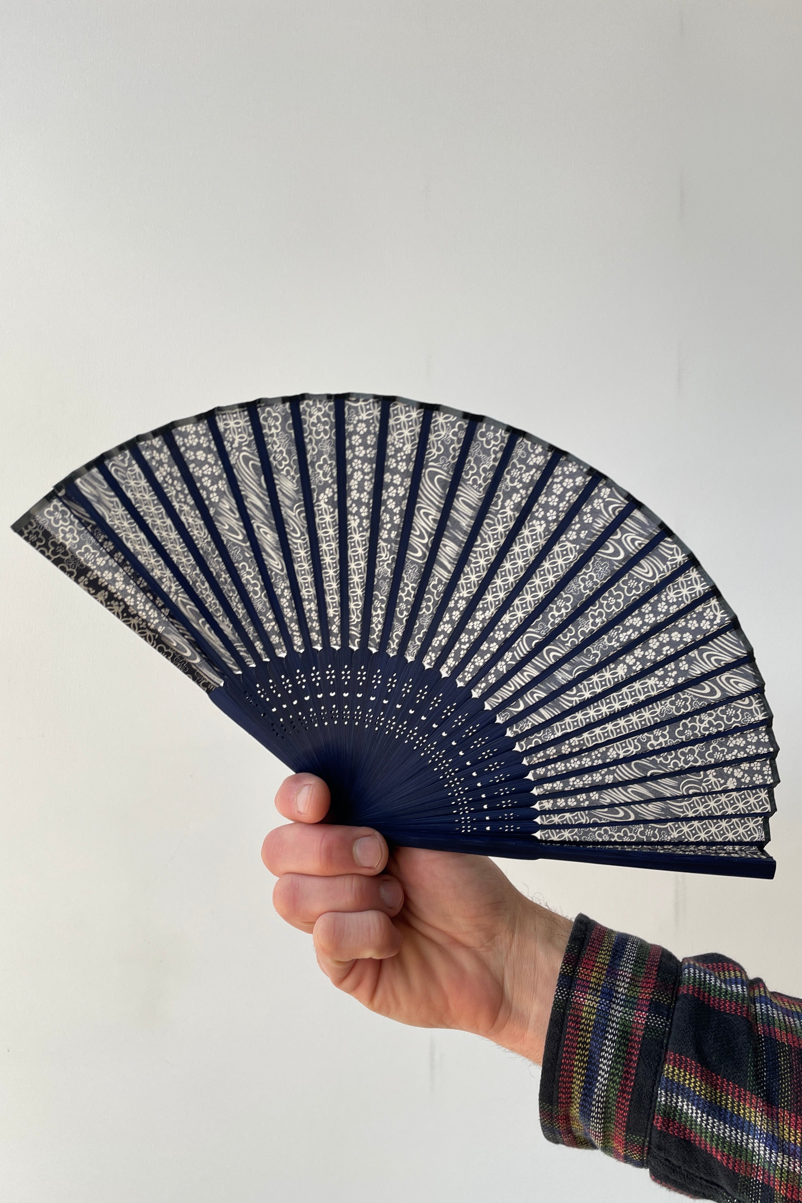 A blue swirl pattern fan with blue bamboo being held in hand against a white backdrop.