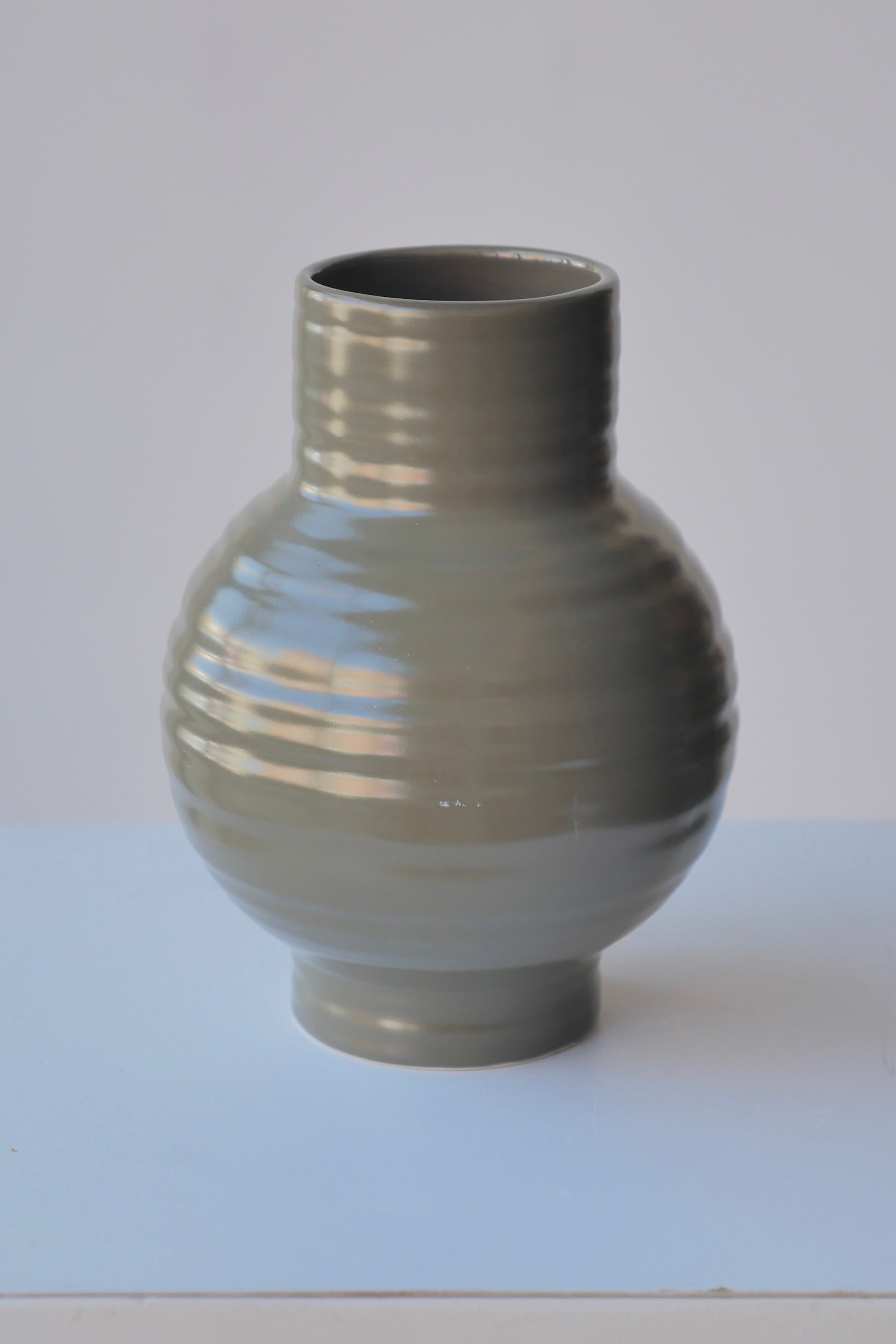 The Small Olive Essential Hawkins Vase against a white wall.