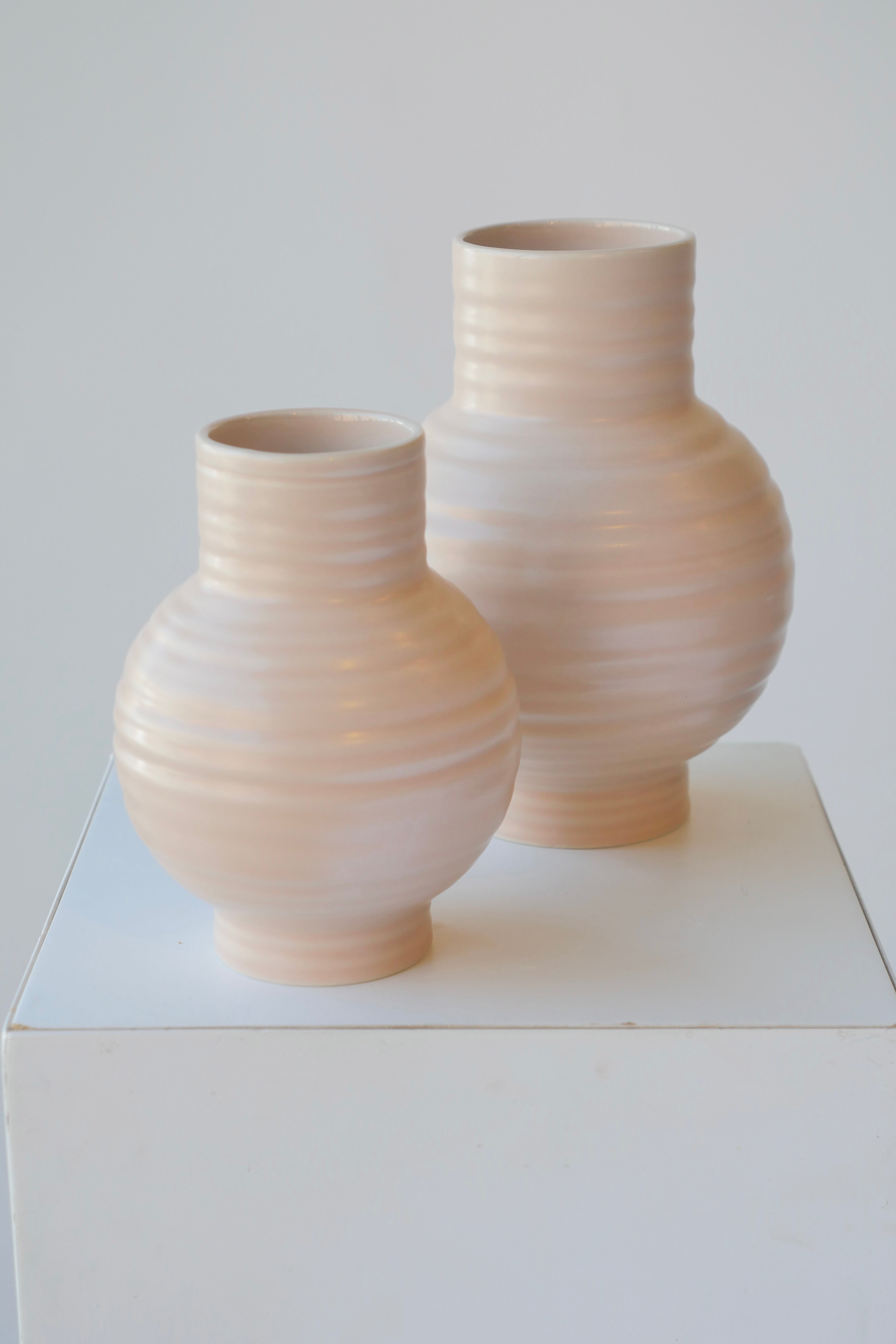 A par of large and small Essential blush vases on white.