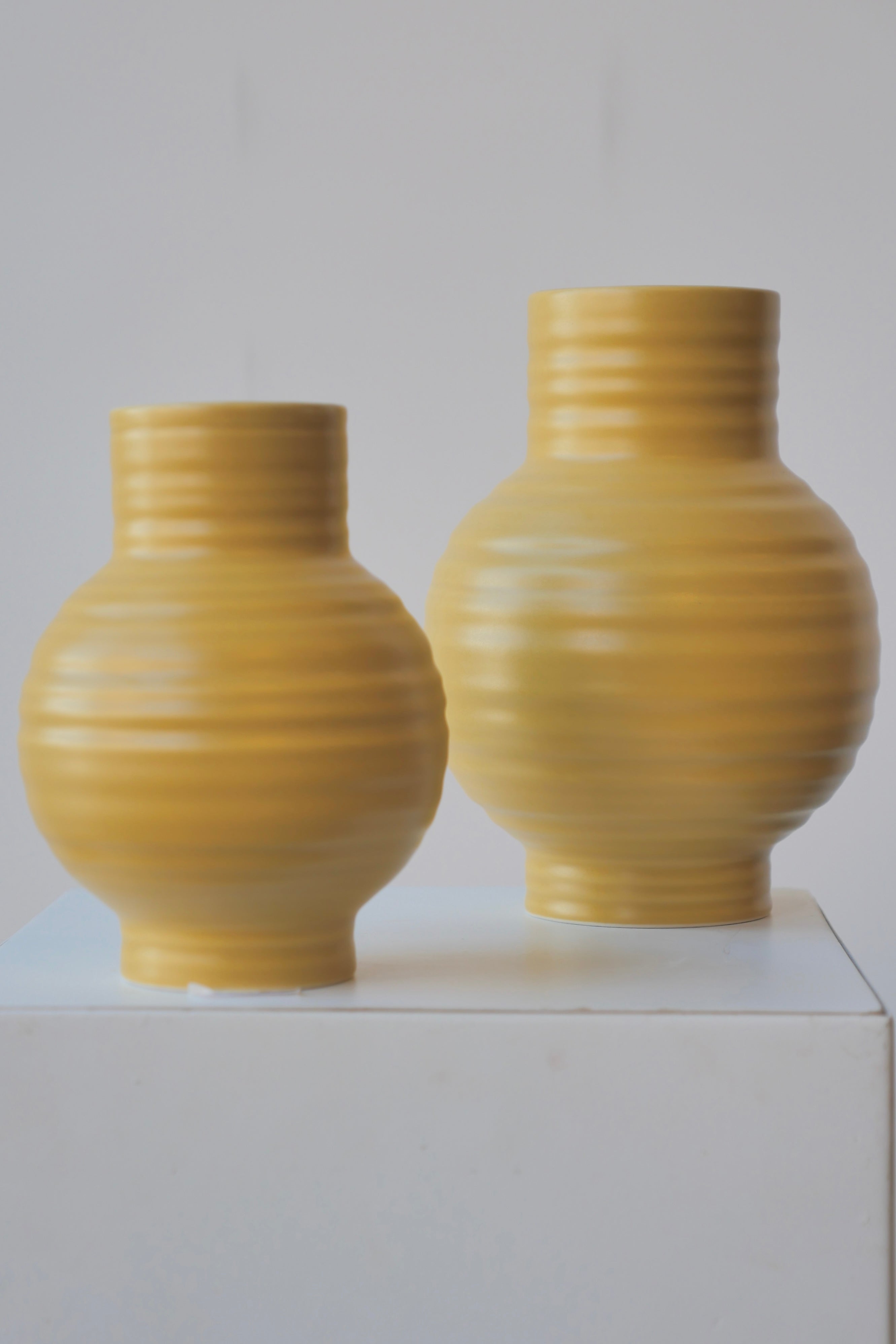 A pair of Mustard Essential Vases by Hawkins NY against a white wall.