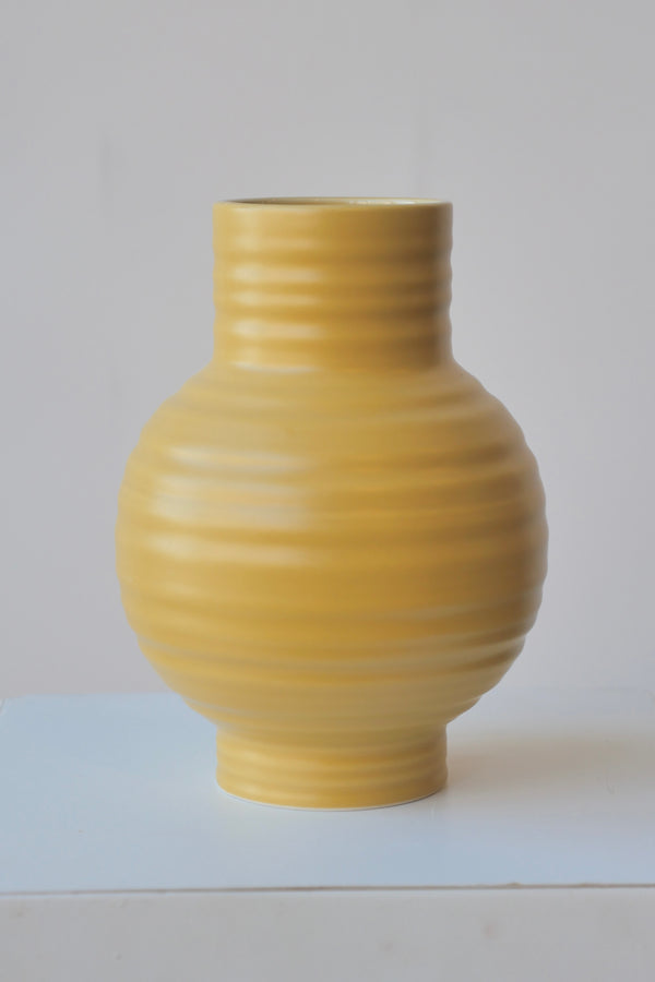 Mustard colored Essential vase by Hawkins at eye level against a white background.
