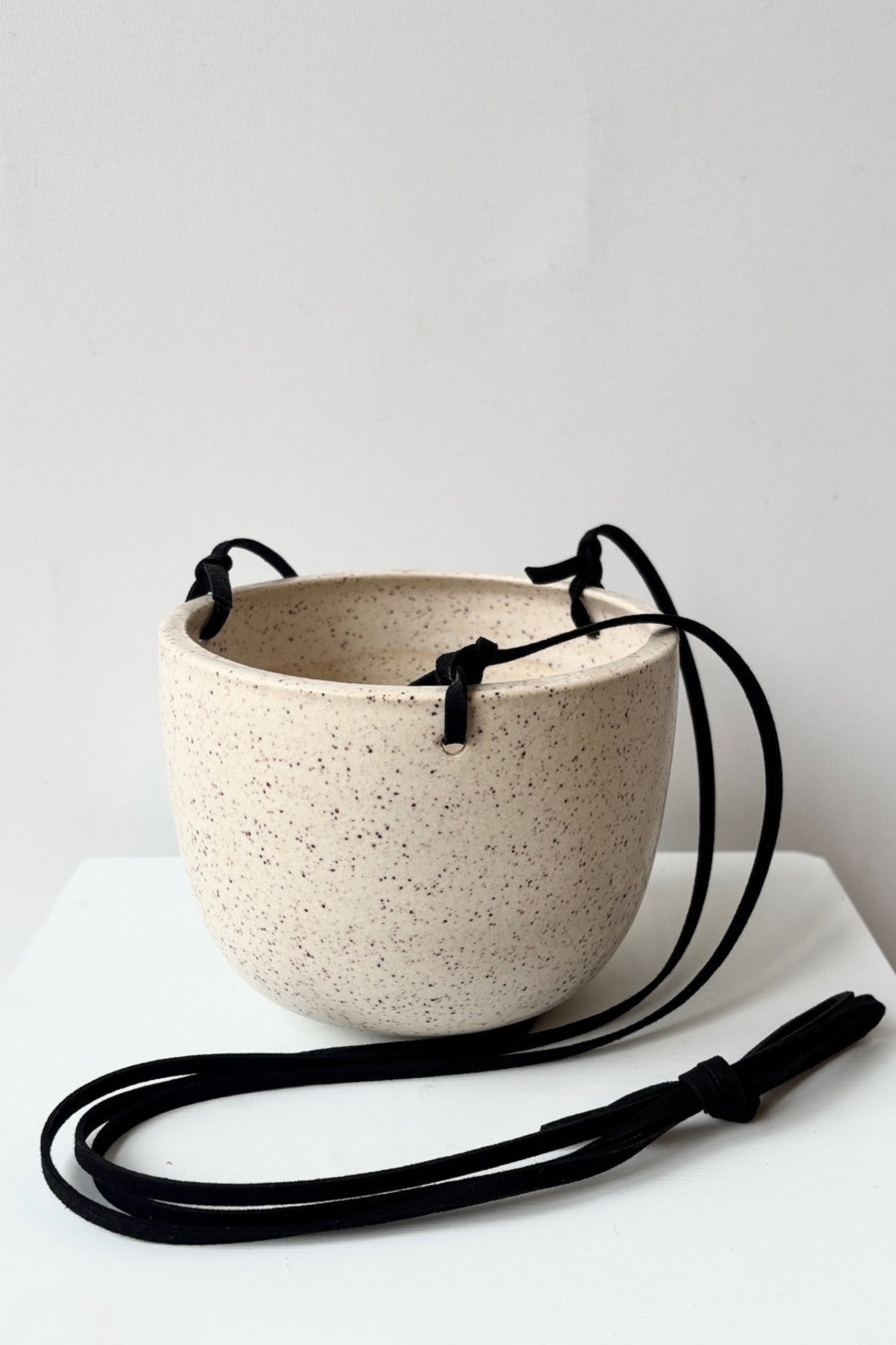 Speckled ceramic hanging bowl with black cord on a white surface ©Sprout Home