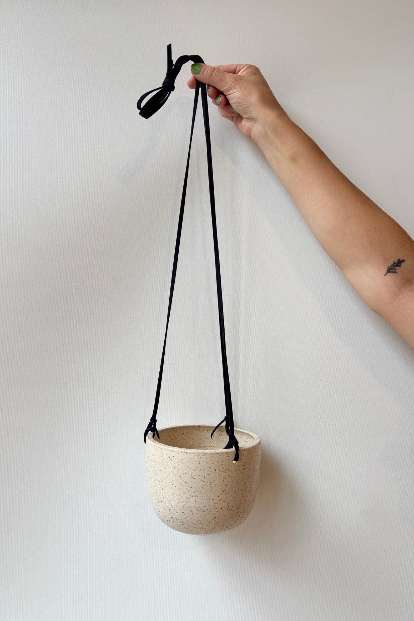Hand holding a cream and speckled hanging planter with black strap against a plain background ©Sprout Home