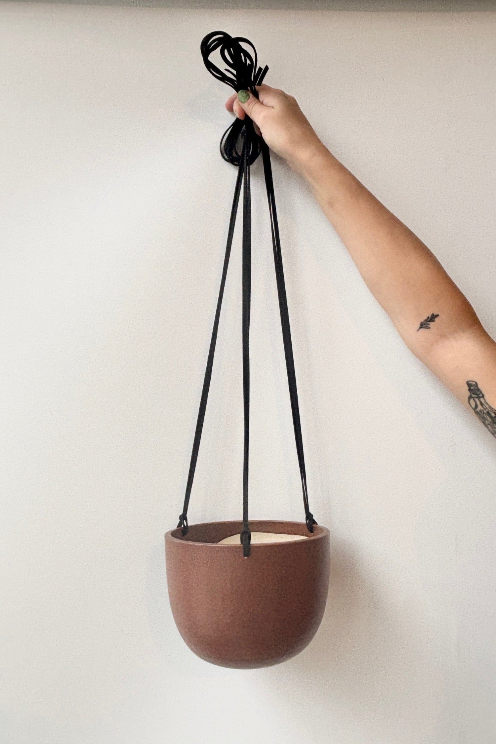 Person holding a brown hanging plant pot with black speckles and a black cord against a white wall ©Sprout Home