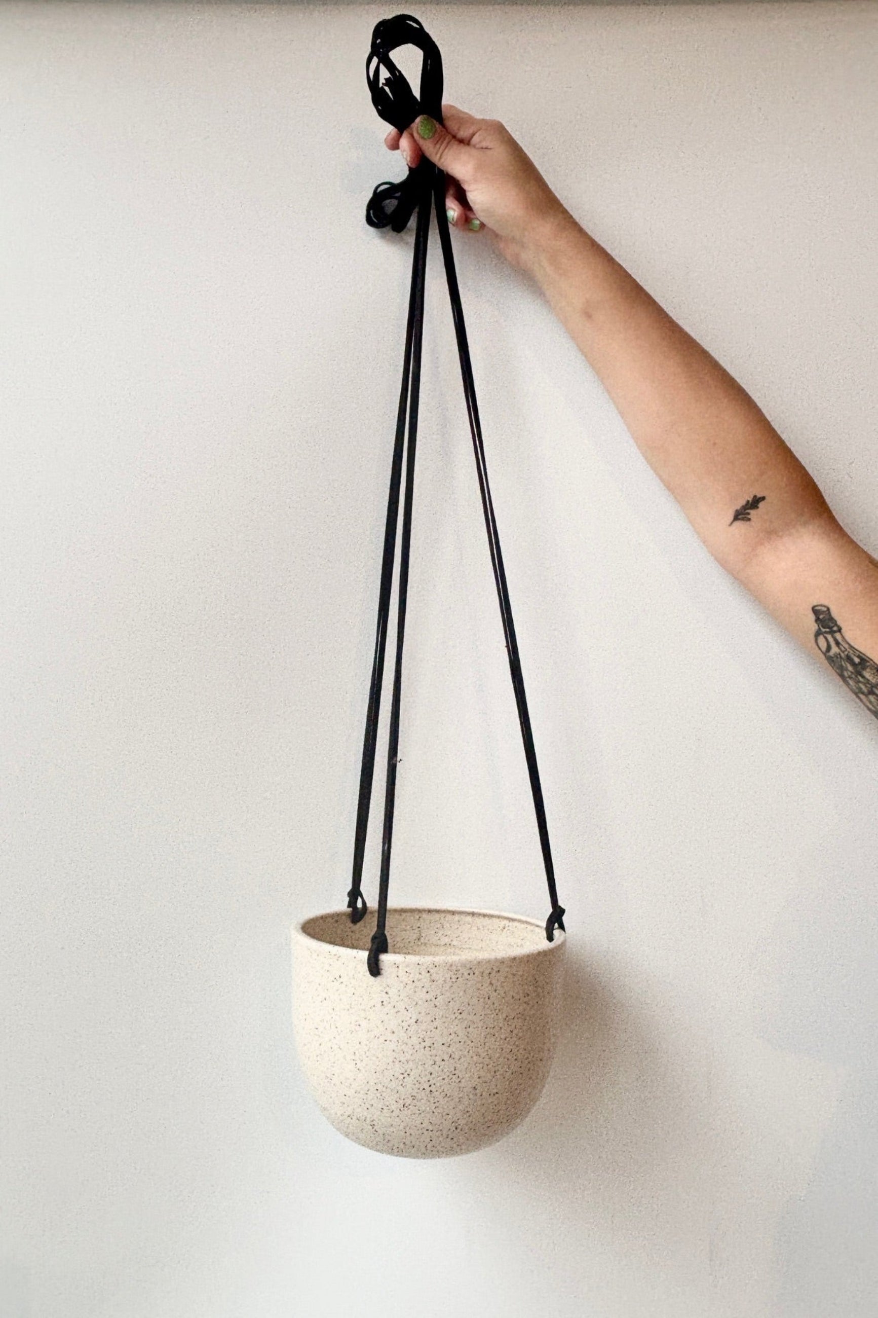 Hand holding a speckled cream hanging planter with a black cord against a white background ©Sprout Home