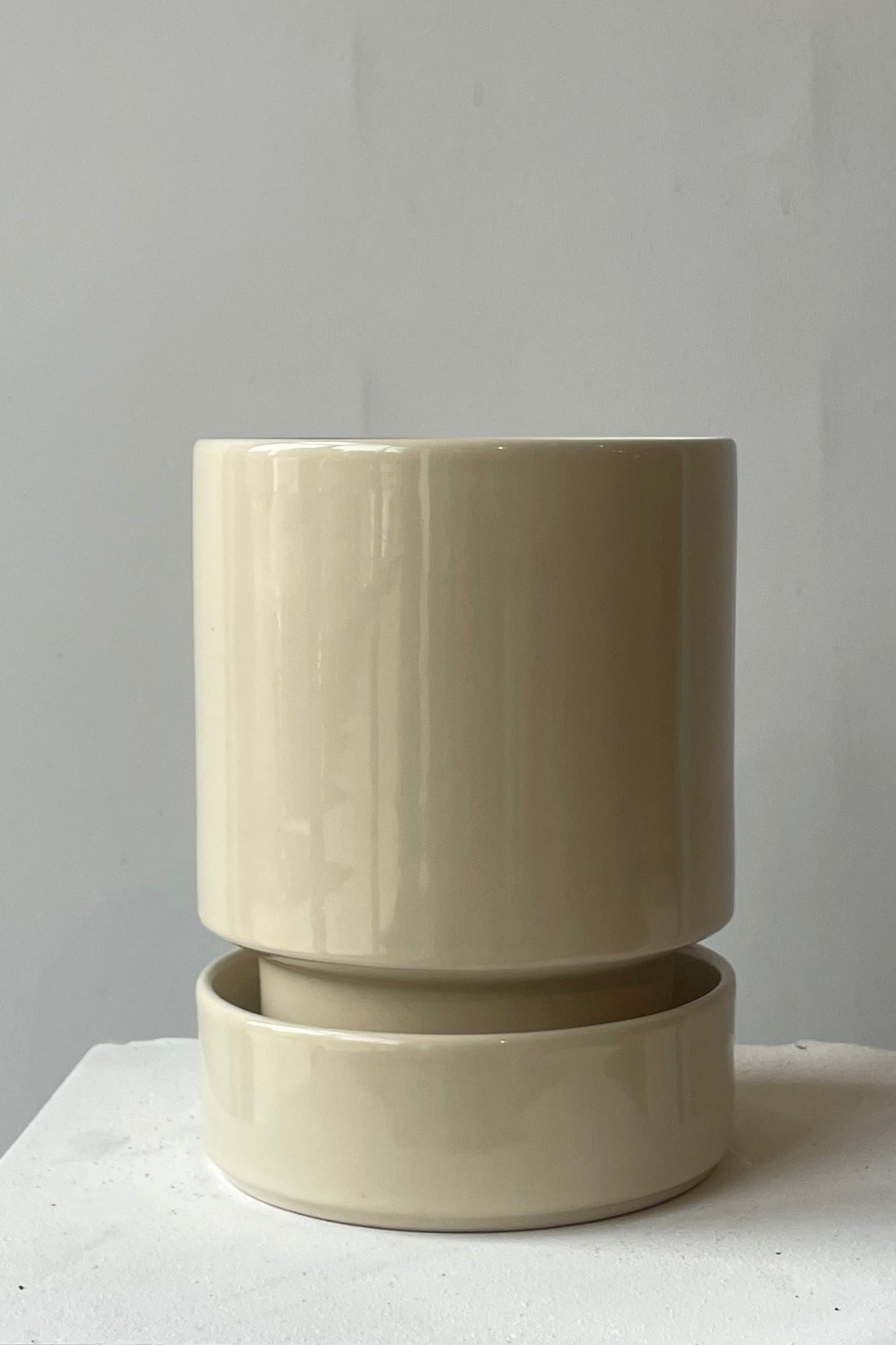 A beige ceramic pot and saucer in a white room. Sandstone Hoff pot by Bergs Potter shown from the front. ©Sprout Home