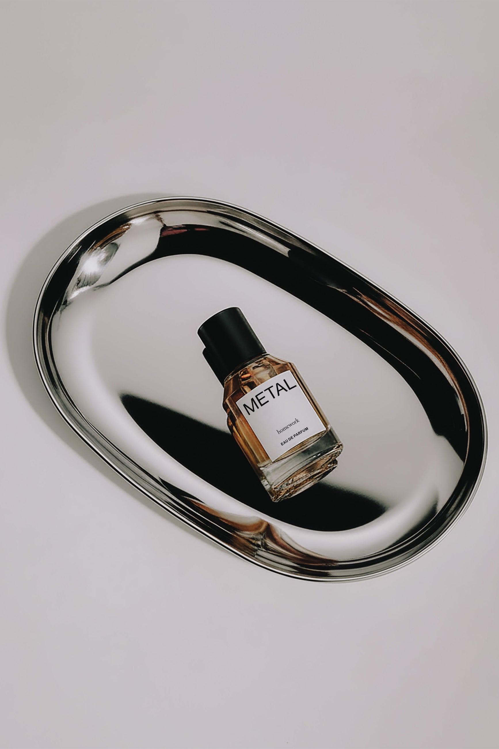 Perfume bottle labeled 'METAL' on a reflective metallic surface with a white background ©Homework