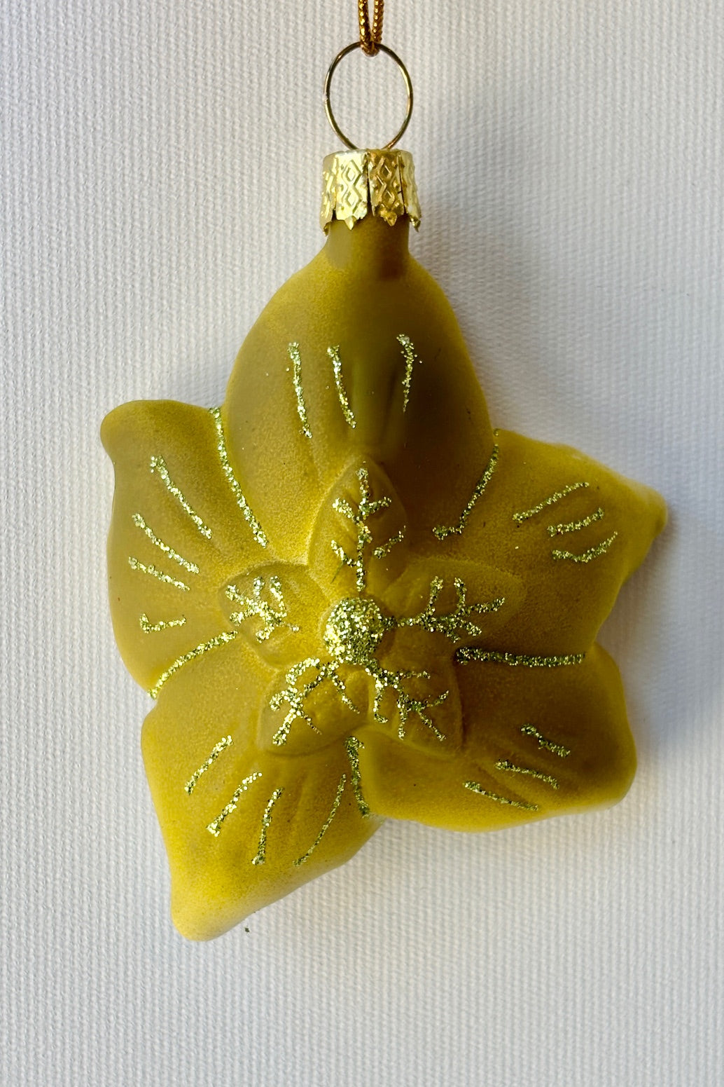 Backside of the Helleborus ornament painted in a pale green with gold glitter accents against a white wall. ©Sprout Home