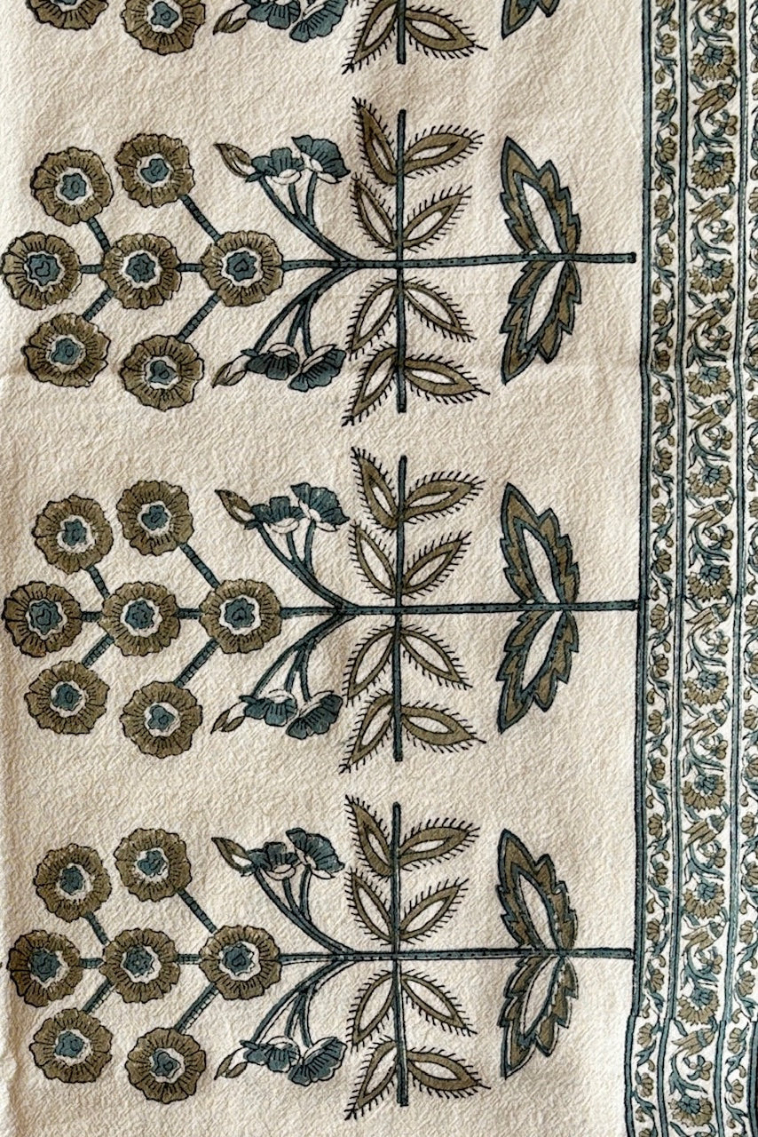 One hundred percent cotton runner with repeating florla motif in teal and gold on an off white fabric bordered by a smaller floral motif in the same color along the edges.