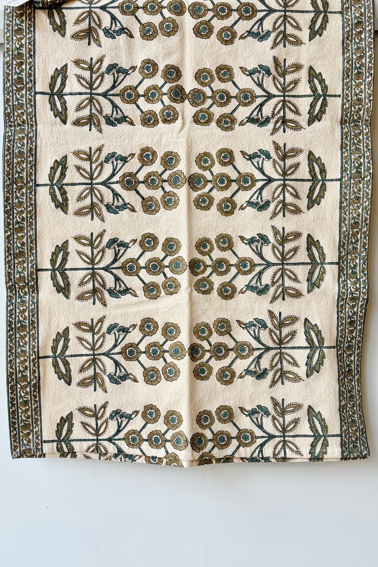 One hundred percent cotton table runner with a teal and gold floral motif arranged in a symmetrical pattern with a border of smaller floral patterns at the edges.