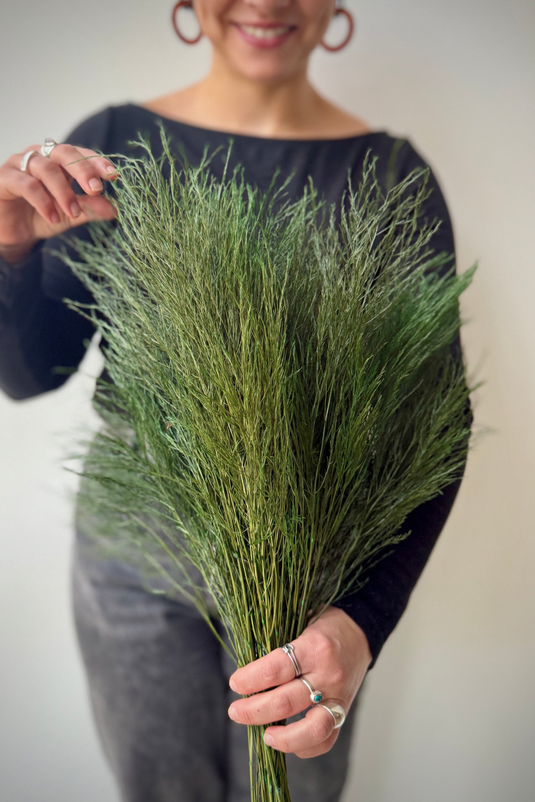 Sprout staff member holding a bundle of preserved asparagus fern greenery against a neutral background ©Sprout Home