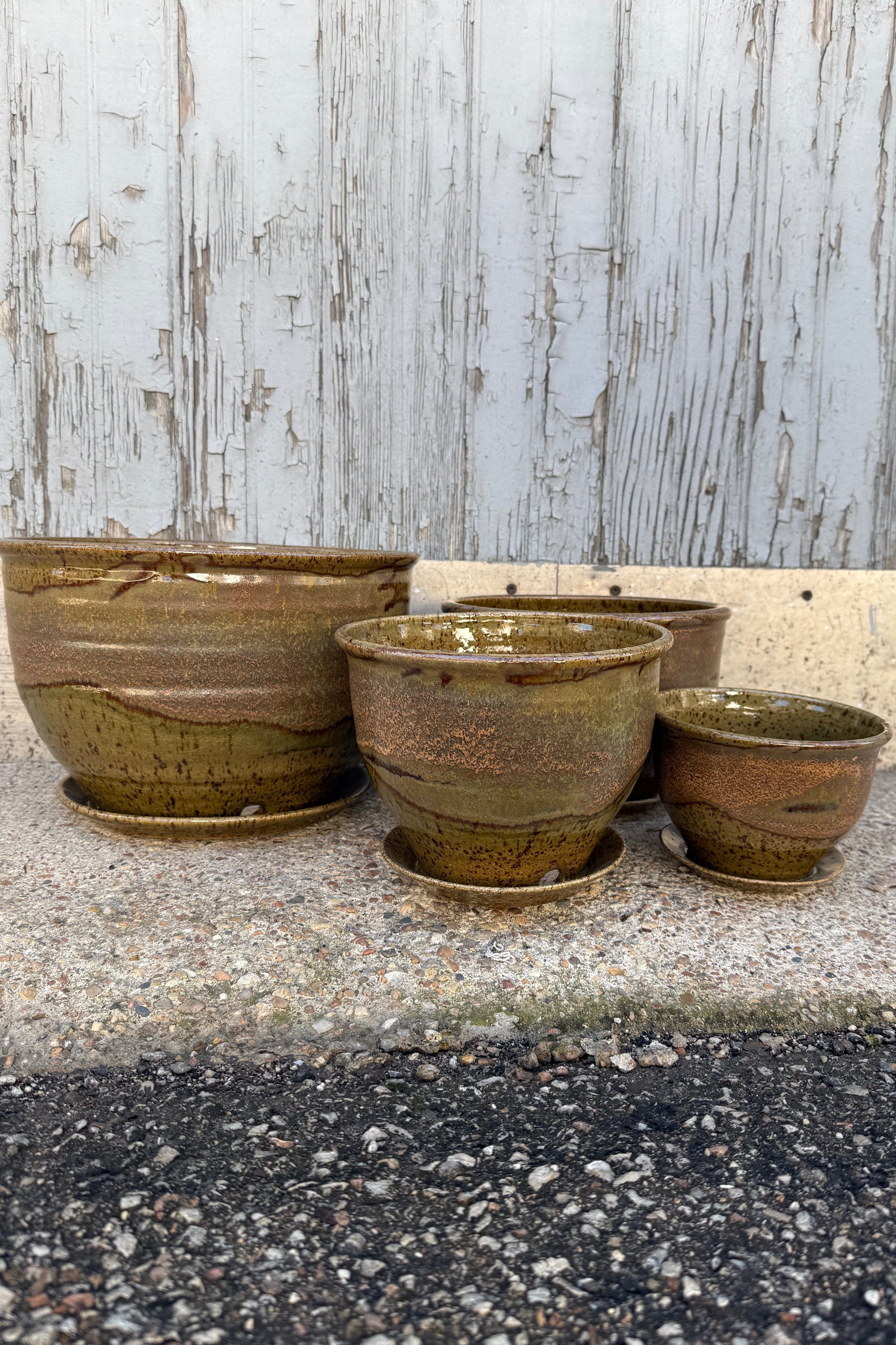 a series of various sized ceramic Bruning pots in an Army Green with Yellow speckled glaze on a stone surface. ©Sprout Home