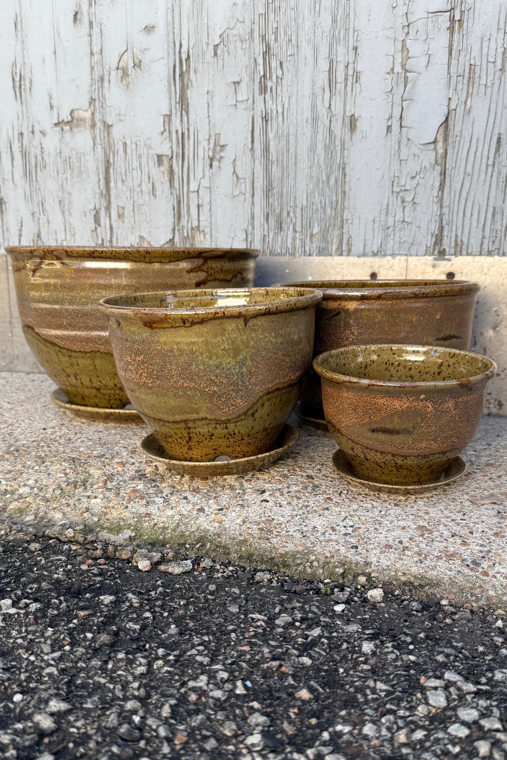 A series of various sized ceramic Bruning pots in an Army Green with Yellow speckled glaze on a stone surface. ©Sprout Home