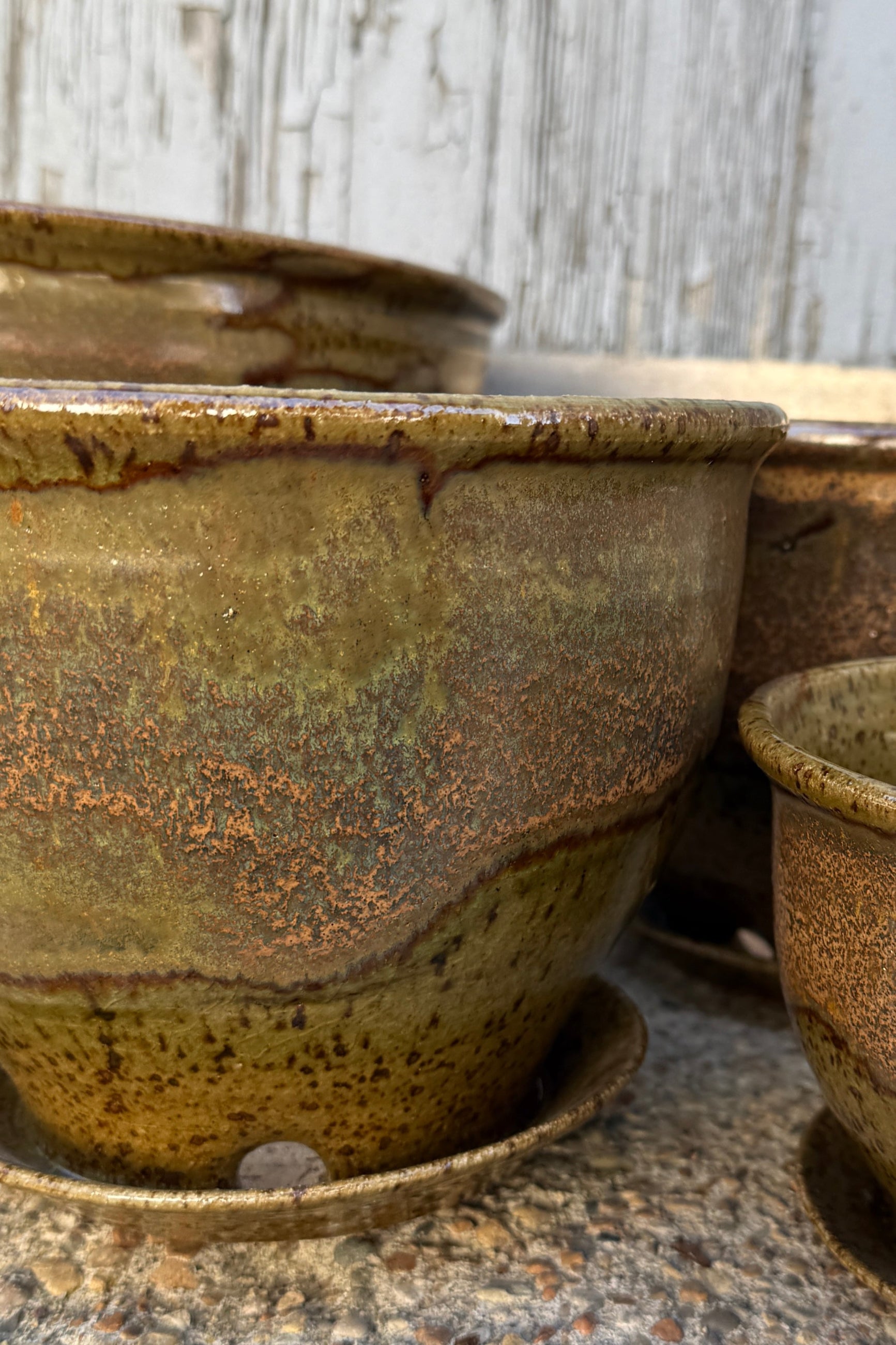Three ceramic Bruning pots in an Army Green with Yellow speckled glaze on a stone surface. ©Sprout Home