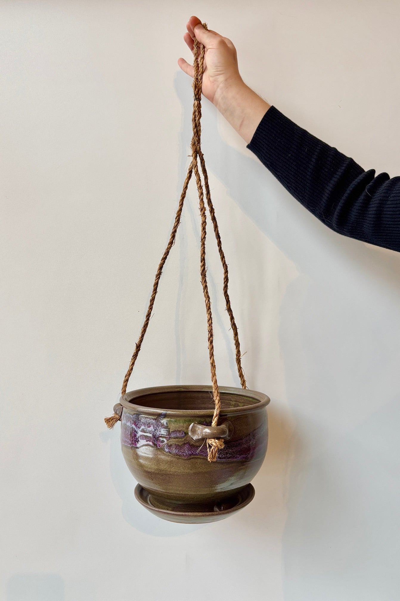 Bruning Pottery 8" Hanging Planter moss & lilac glaze with shades of brown, lavender and green held in front of white wall