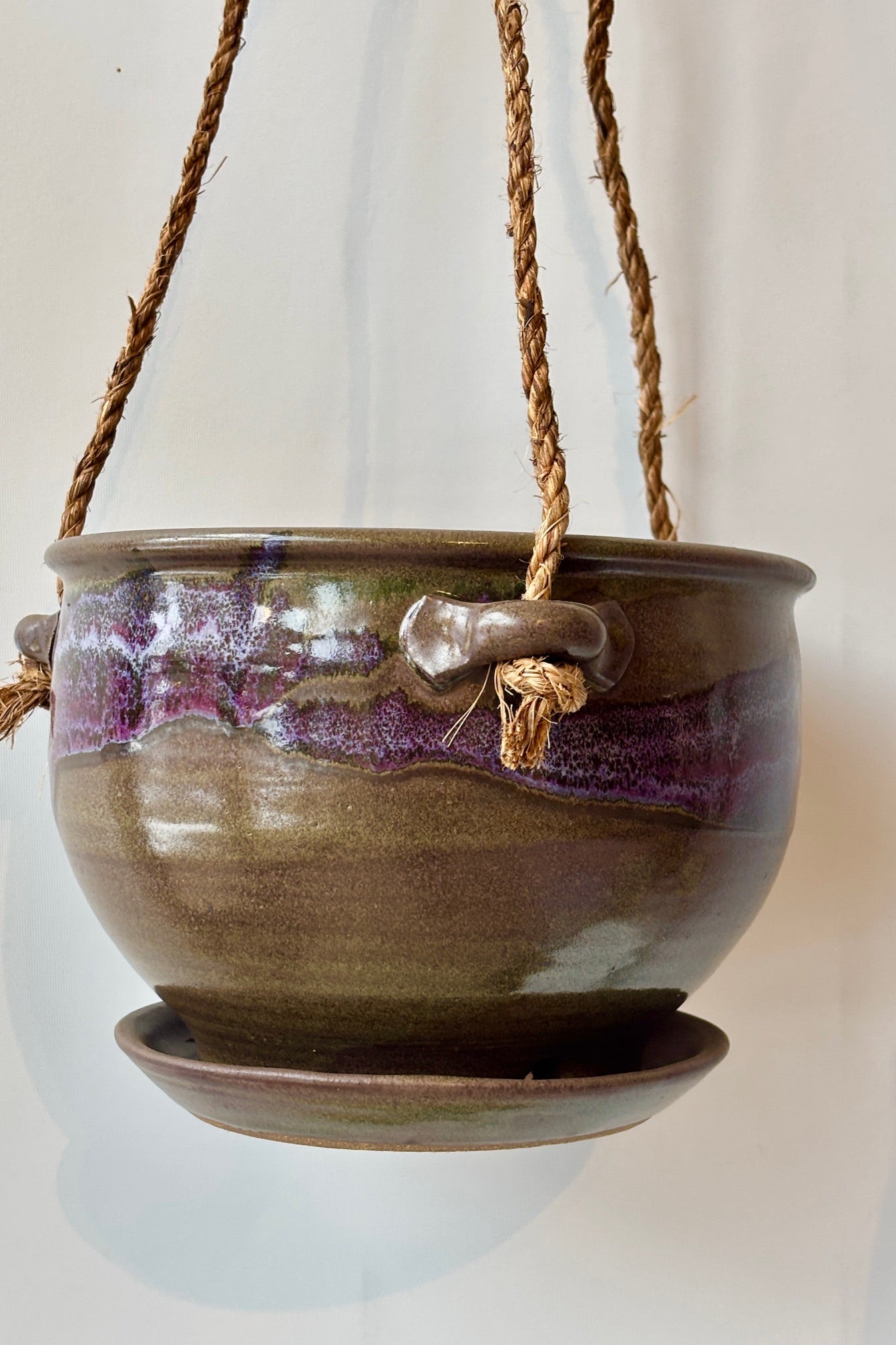 Bruning Pottery 8" Hanging Planter moss & lilac glaze with shades of brown, lavender and green held in front of white wall