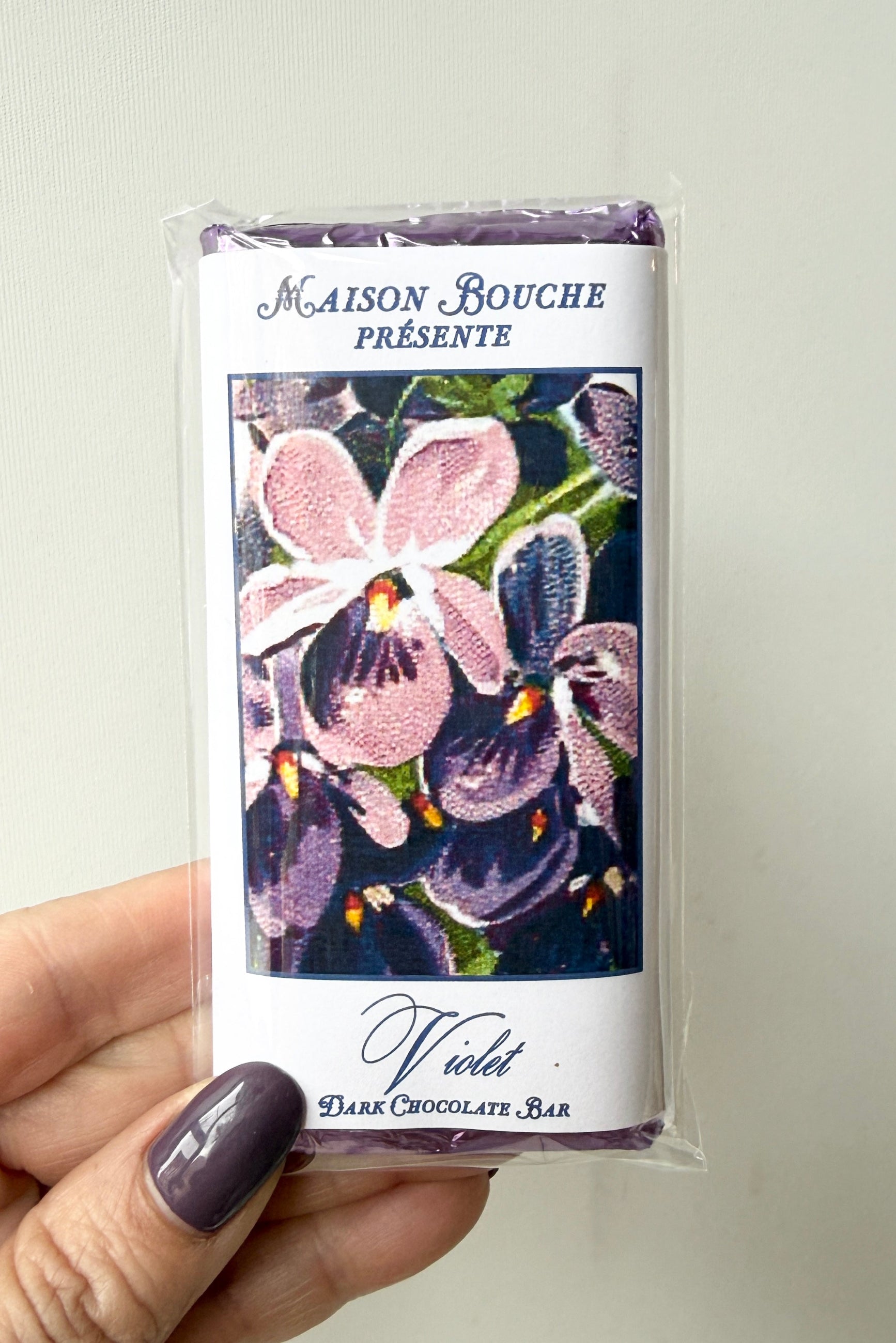 Maison Bouchee Violet Dark Chocolate Bar packaging held by a hand with purple nail polish. ©Sprout Home