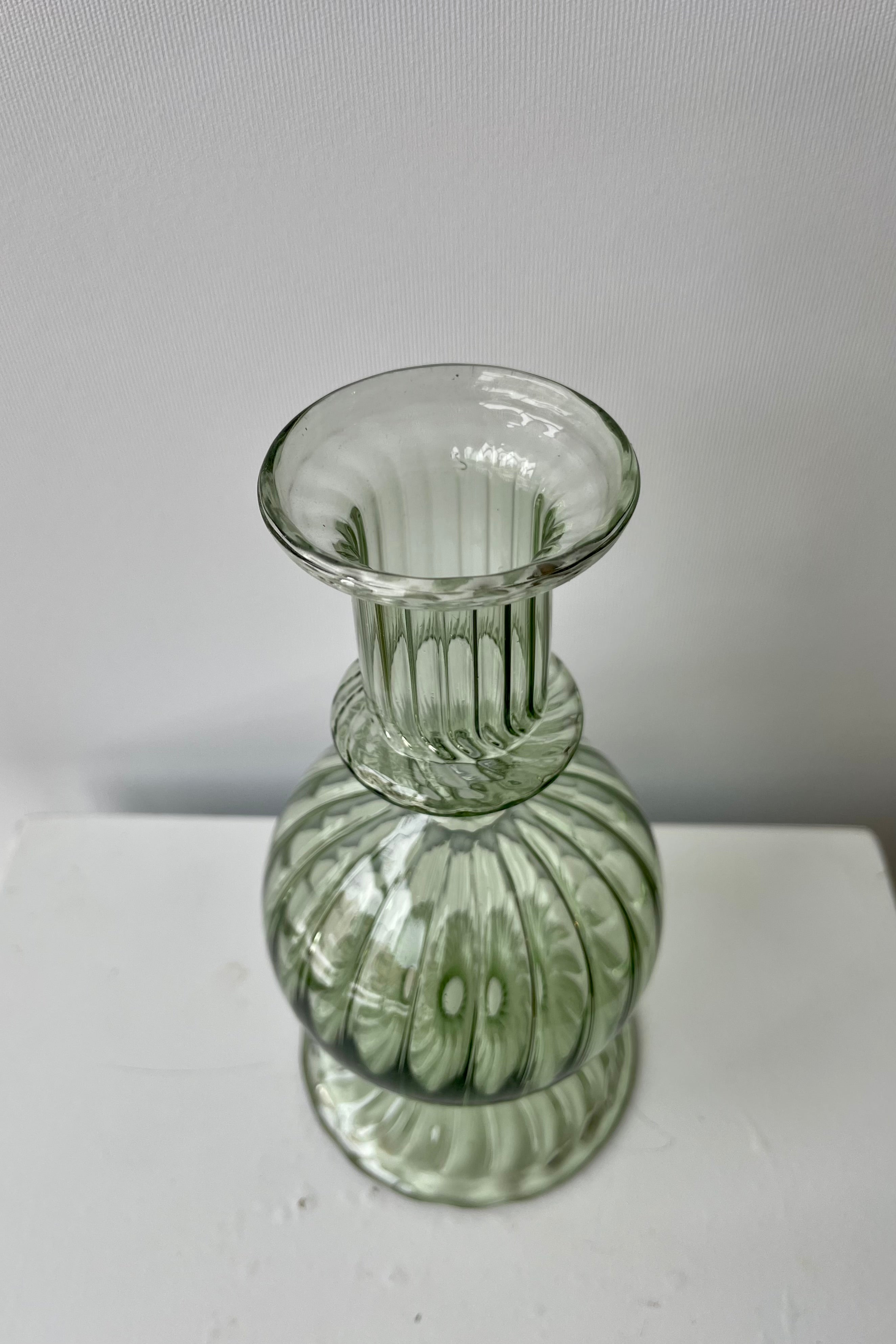 Photo from above of green transparent glass of Nalia Parakeet Candlestick Hollder against a white wall.