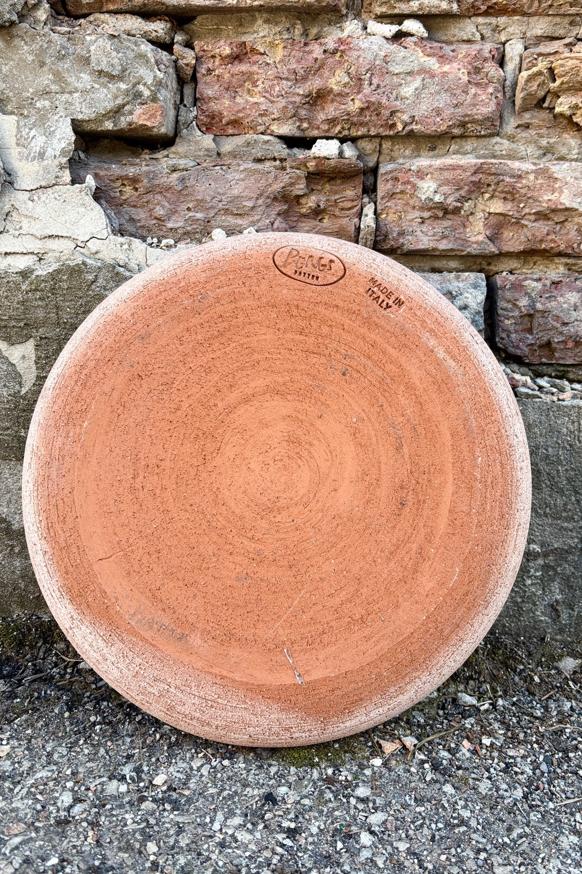Back side of clay saucer for 15.7" Julie pot in color Rosa against an exposed brick wall