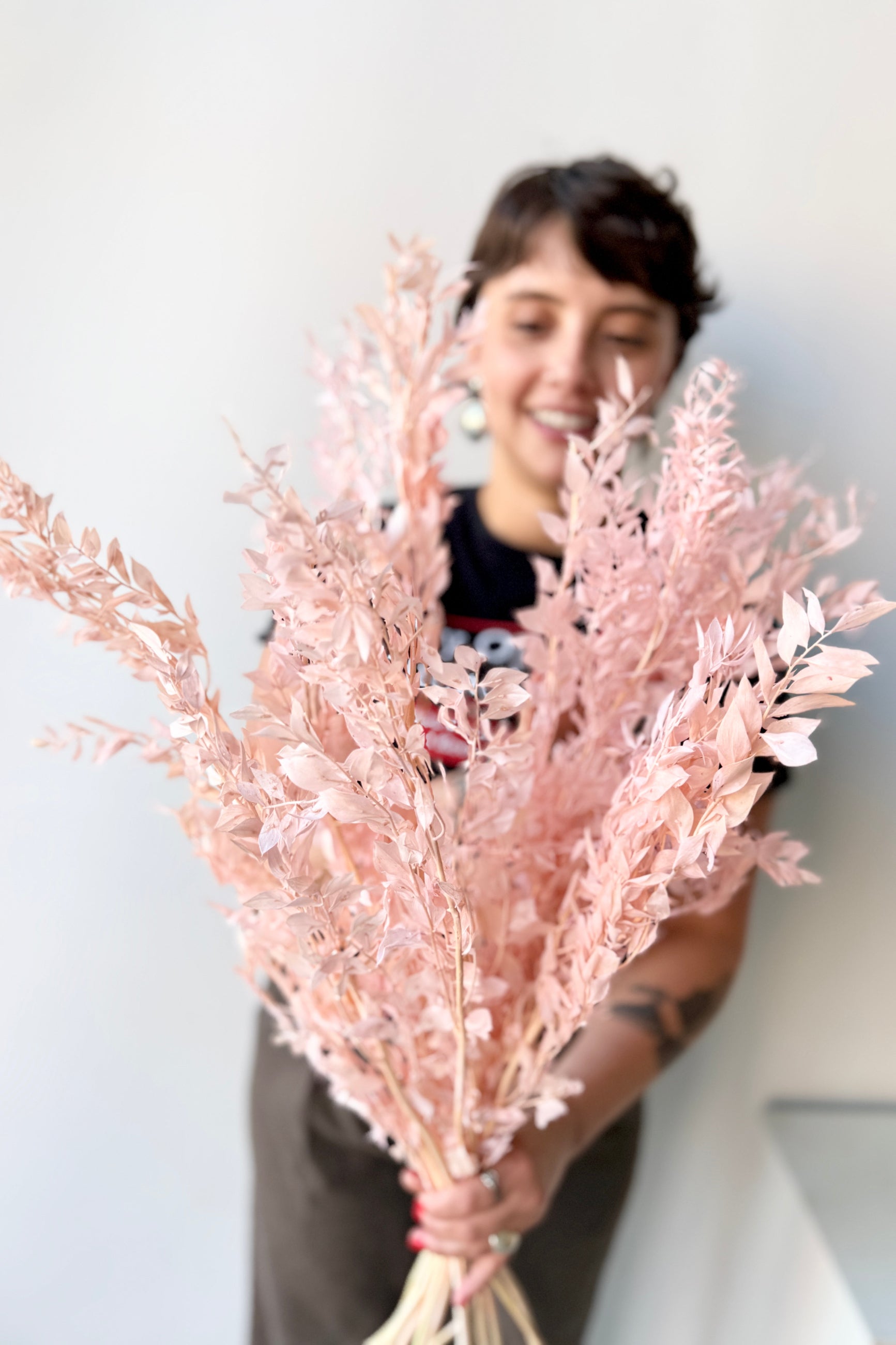 Person holding a bouquet of pink dried Ruscus against a white background ©Sprout Home