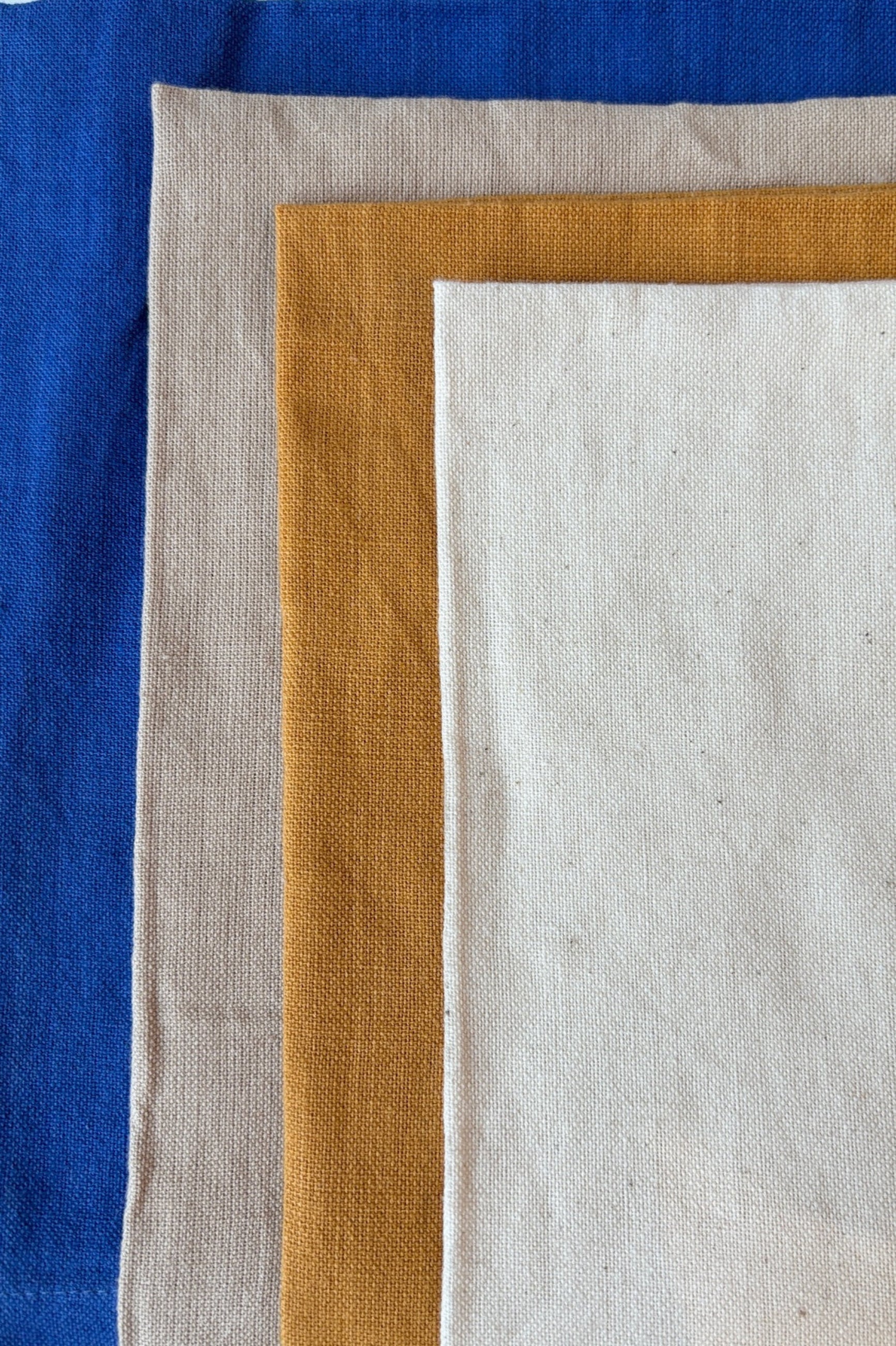 Four colors of 100% cotton, homespun, handwoven napkins in royal blue, sand, mustard, and natural against a white backgound ©Sprout Home
