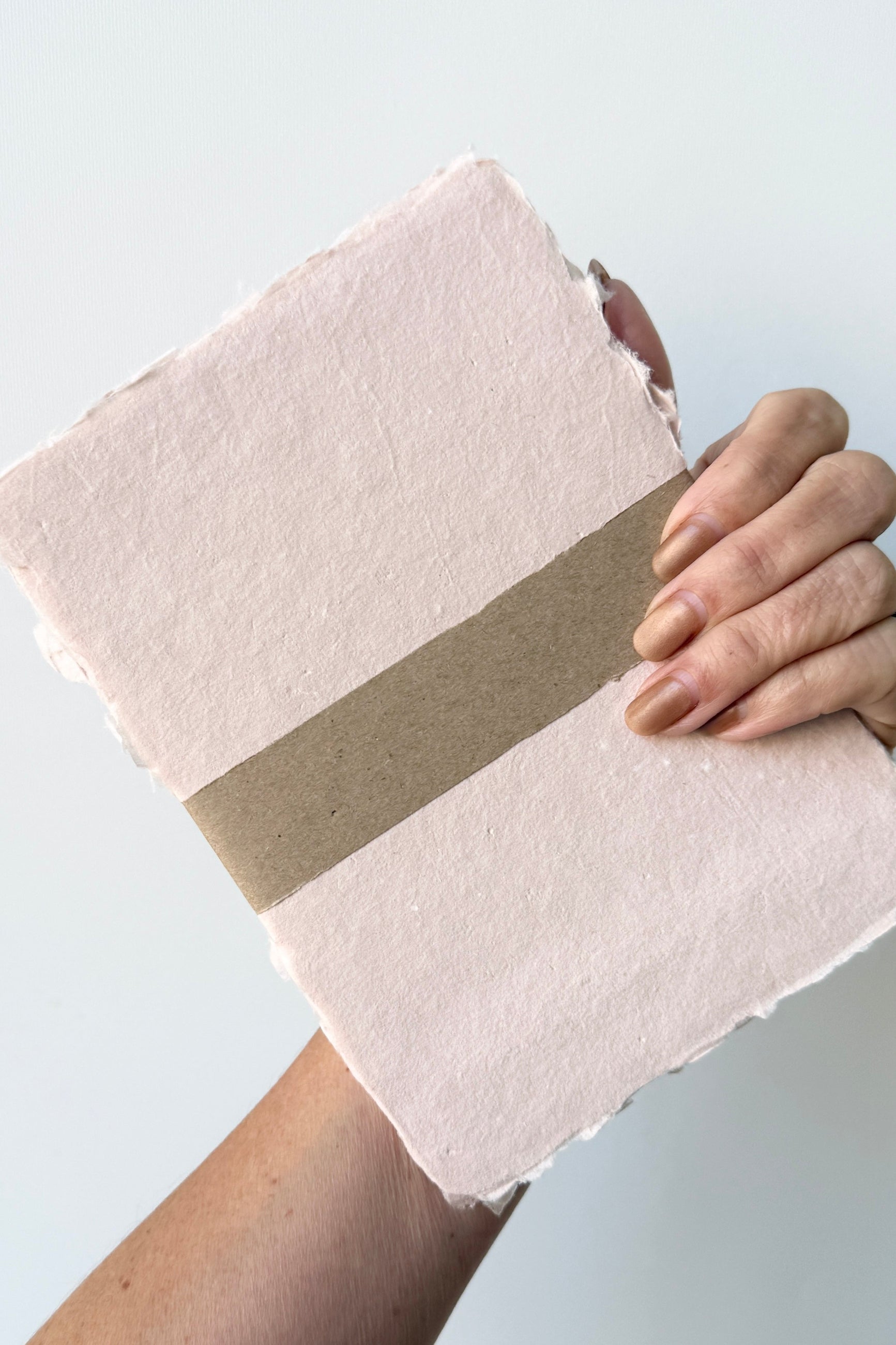 Hand holding a Handmade Blush Paper Sheet Set in 5 x 7" by Sustainable Paper & Craft against a light gray background