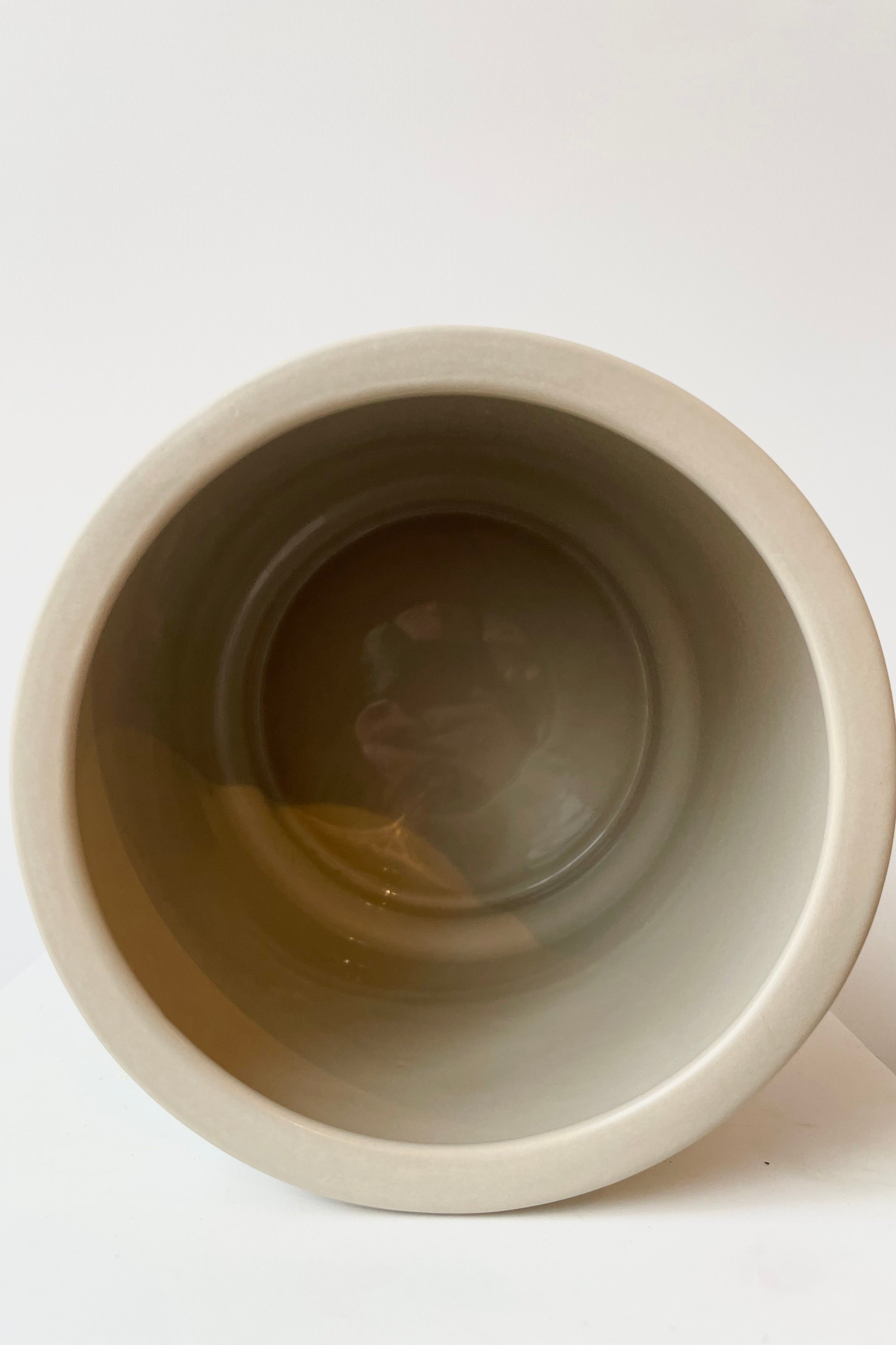 Interior of beige urn shaped ceramic pot no drain hole against white wall