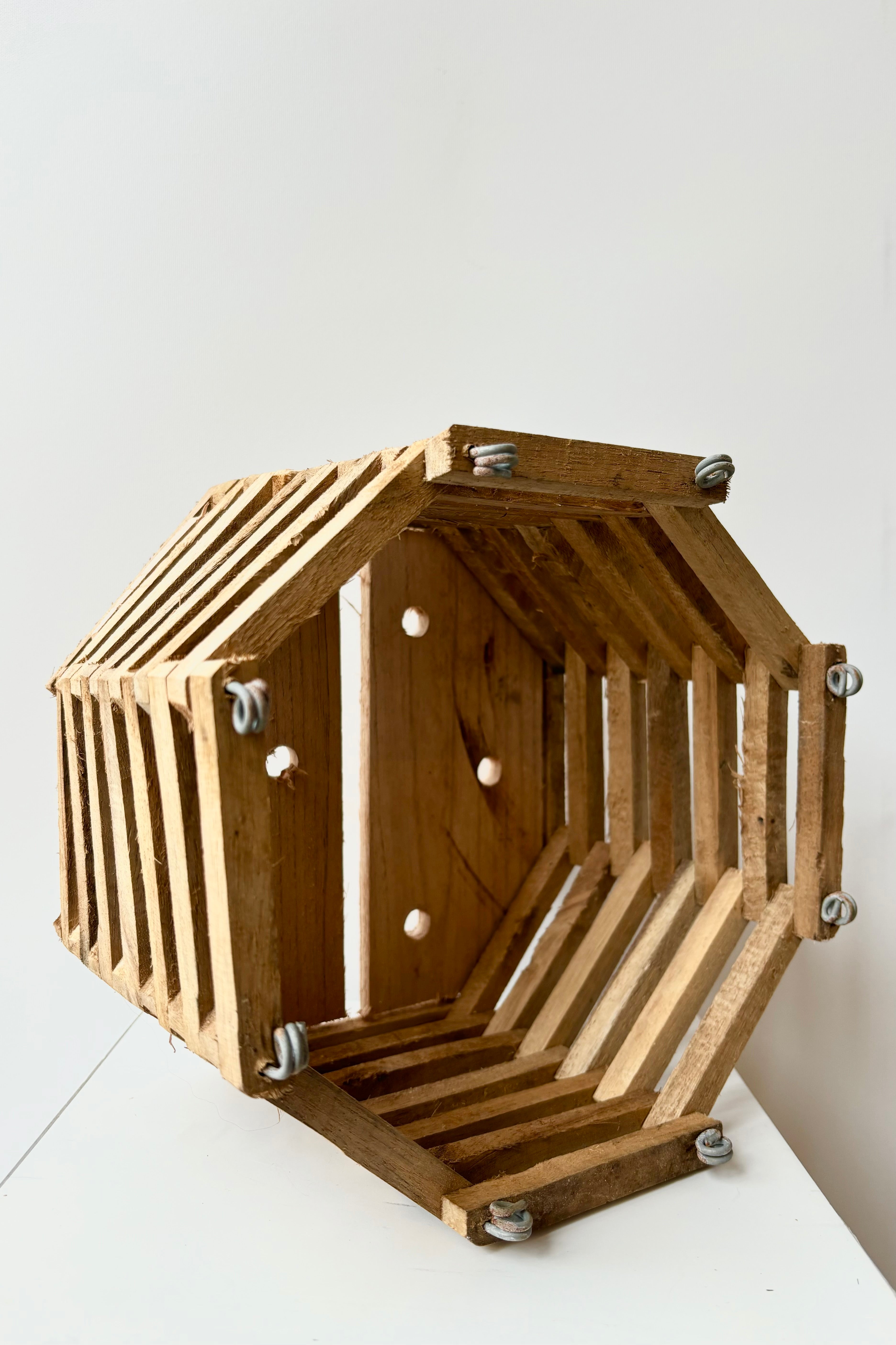 Side view of wooden octangonal slatted basket with metal rings for sting attachment, not included, against white background
