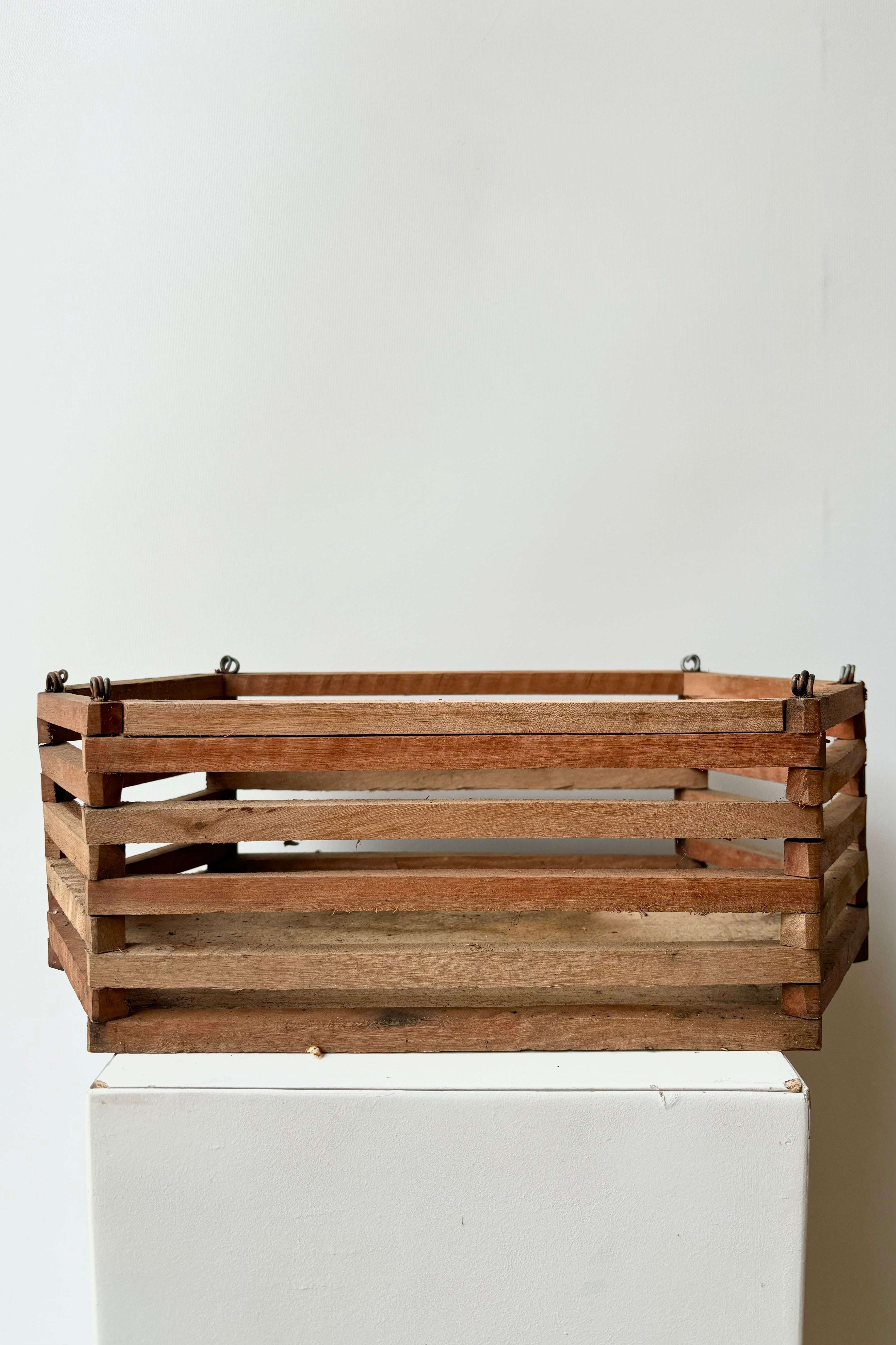 Side view of elongated wooden hexagonal slatted basket with metal rings for string attachment, not included, against white background.