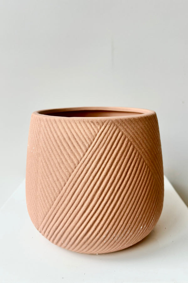 Bare clay terra cotta cachepot with diagonal etching on outside of pot against white background.