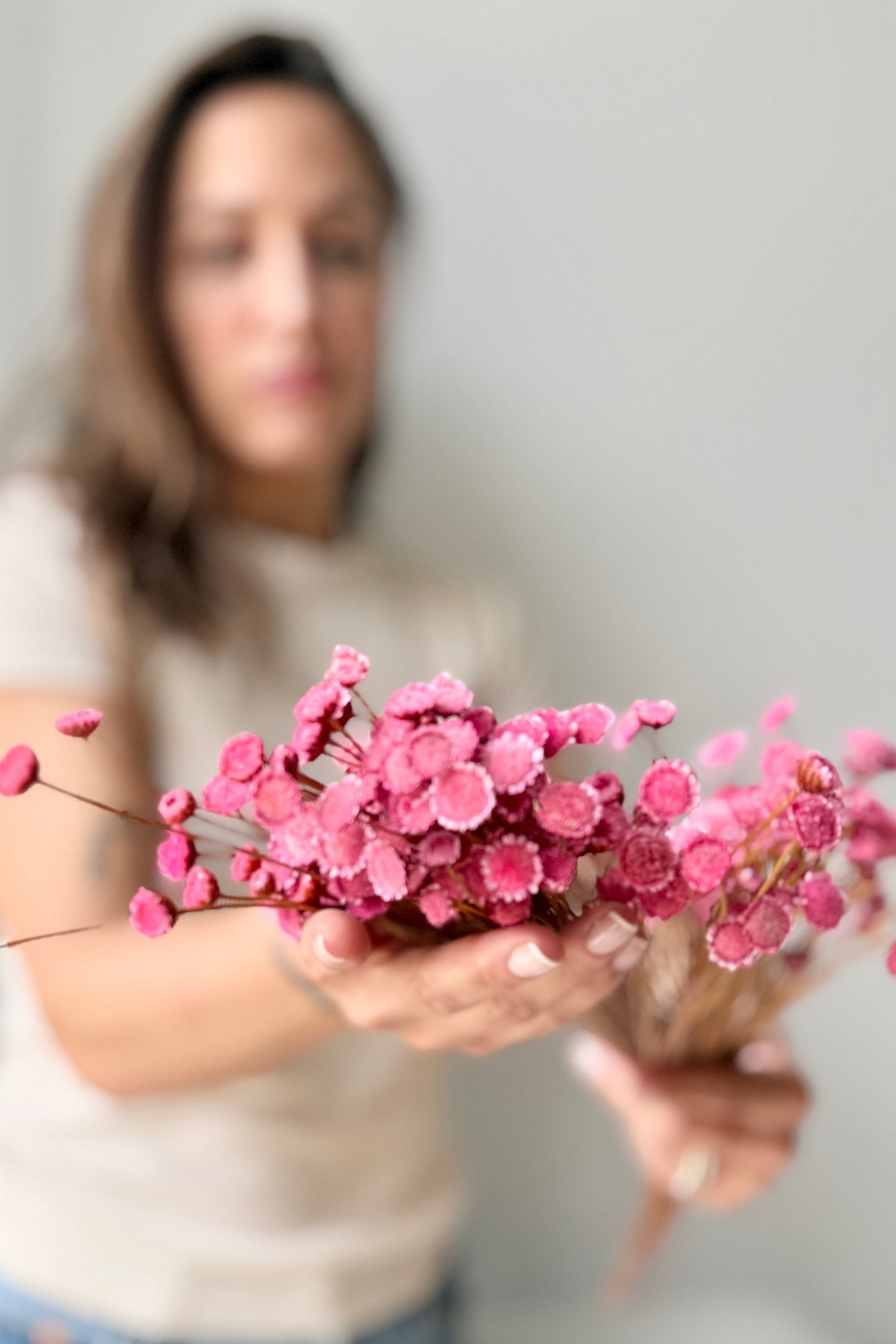 A person holding a Margaret Light Pink Color Preserved Bunch, with the flowers in sharp focus and the person blurred in the background against a light gray wall. ©Sprout Home