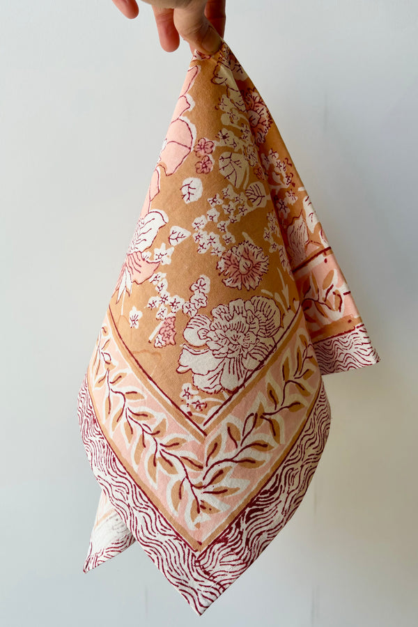Hand block printed Panjim napkin with a gold and pink floral motif with maroon accents against white background.