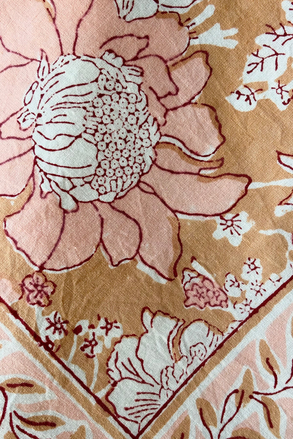 Detail of hand block printed Panjim napkin with a gold and pink floral motif with maroon accents against white background.