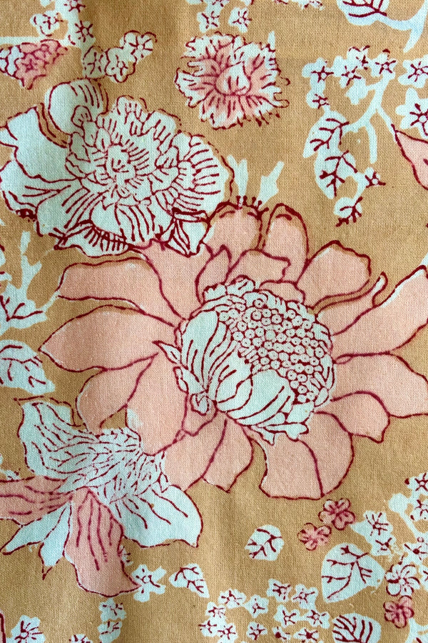 Detail of hand block printed Panjim tablecloth with a gold and pink floral motif with maroon accents.