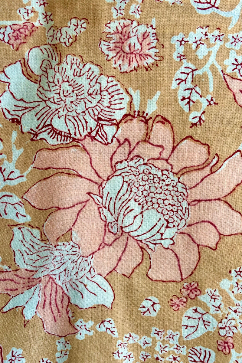 Detail of hand block printed Panjim tablecloth with a gold and pink floral motif with maroon accents.