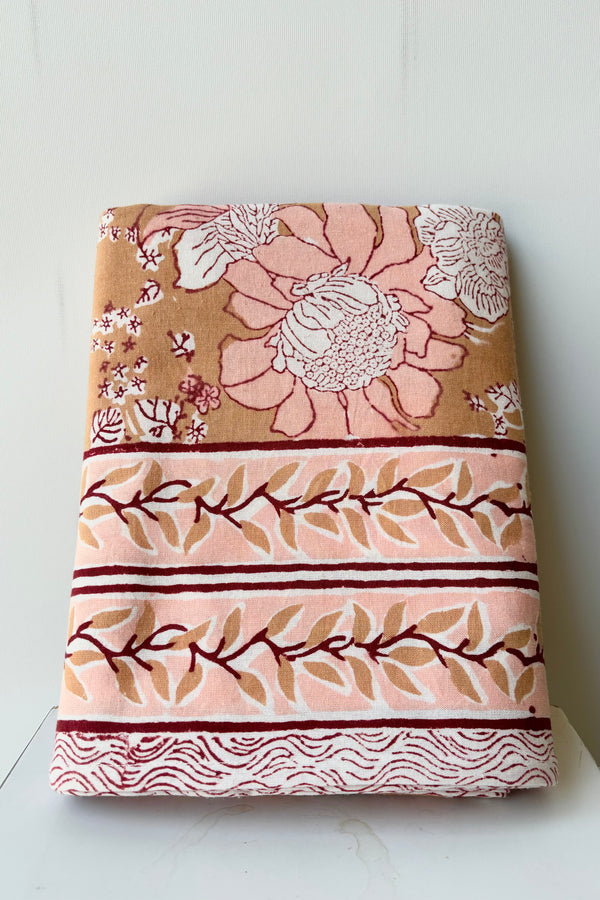 Hand block printed Panjim tablecloth with a gold and pink floral motif with maroon accents against white background.