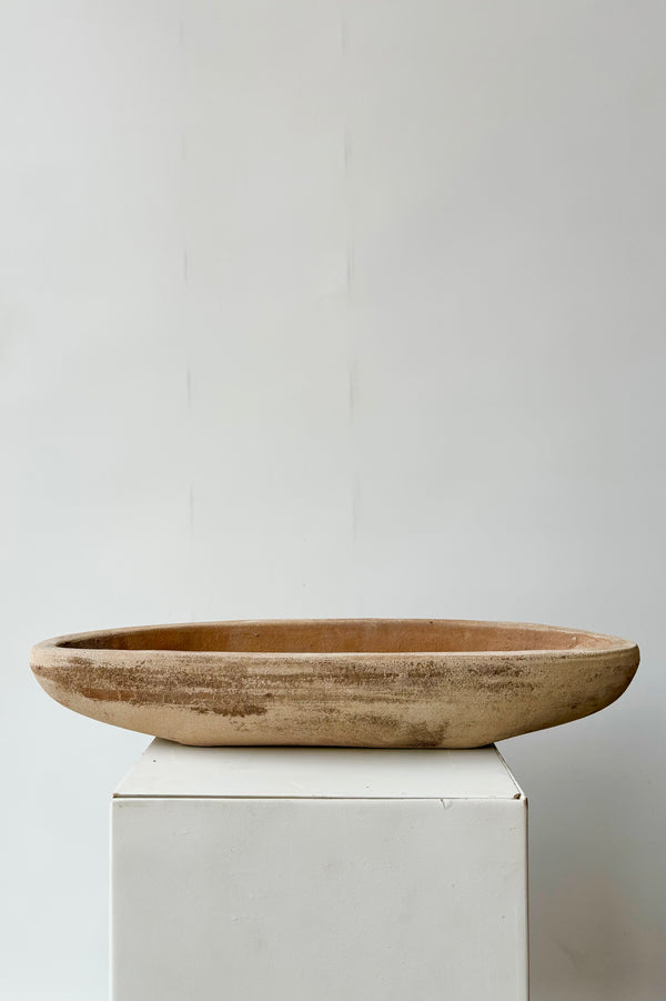 Side view of unrefined oval shaped low clay bowl with drainage hole against white background