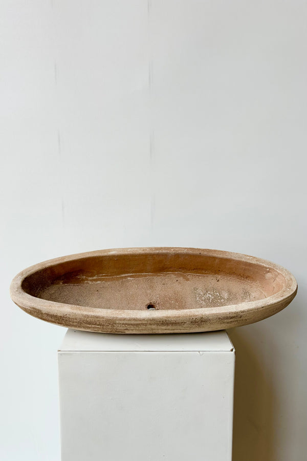 Top view of unrefined oval shaped low clay bowl with drainage hole against white background