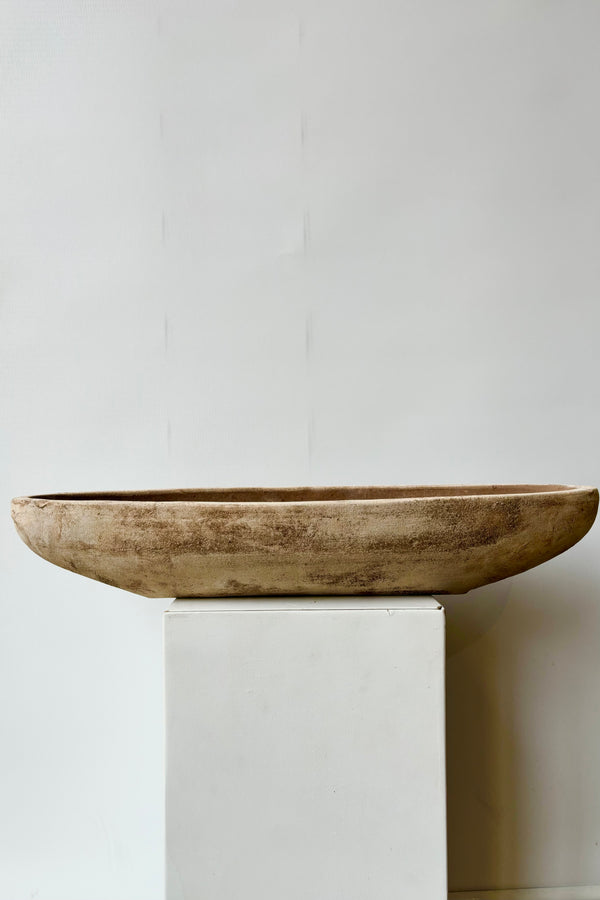Side view of large, unrefined, oval shaped low clay bowl with drainage hole against white background