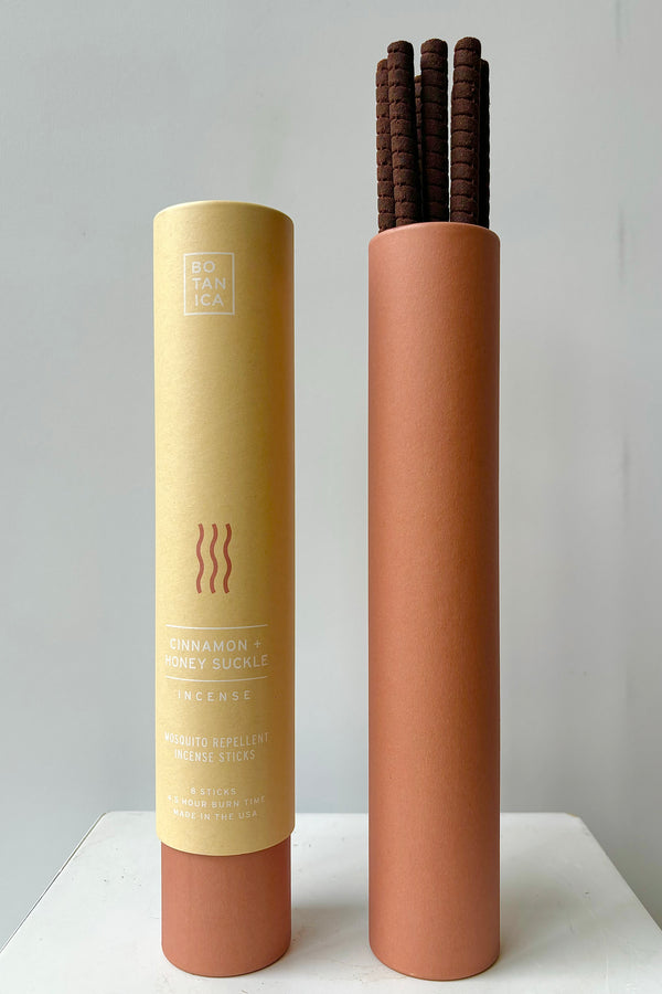 Two kraft paper and salmon colored cardboard tubes showing front of packaging and interior with cinnamon and honeysuckle incense sticks against white wall
