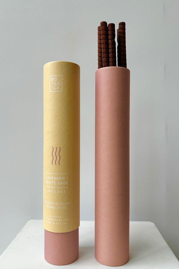 Two kraft paper and mauve colored cardboard tubes showing front of packaging and interior with lavender and white sage incense sticks against white wall