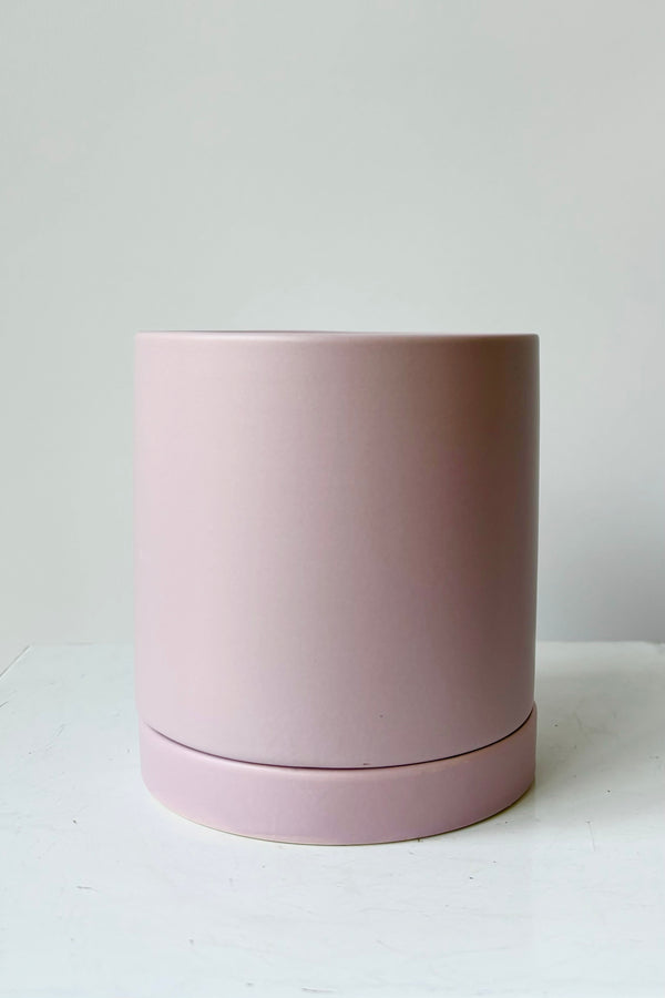 Ceramic, lilac colored glazed cylinder planter with drainage hole and tray against grey background