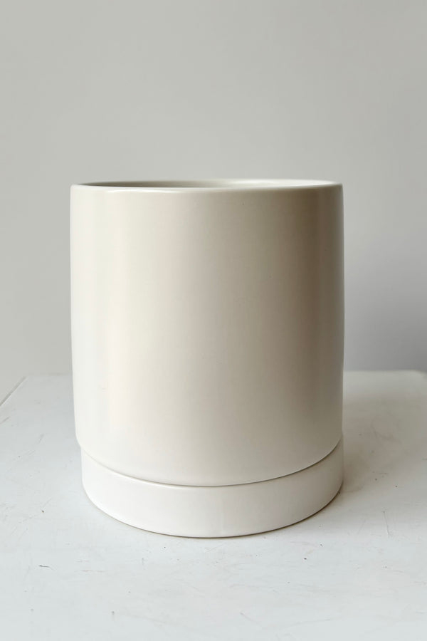 Ceramic, white glazed cylinder planter with drainage hole and tray against grey background