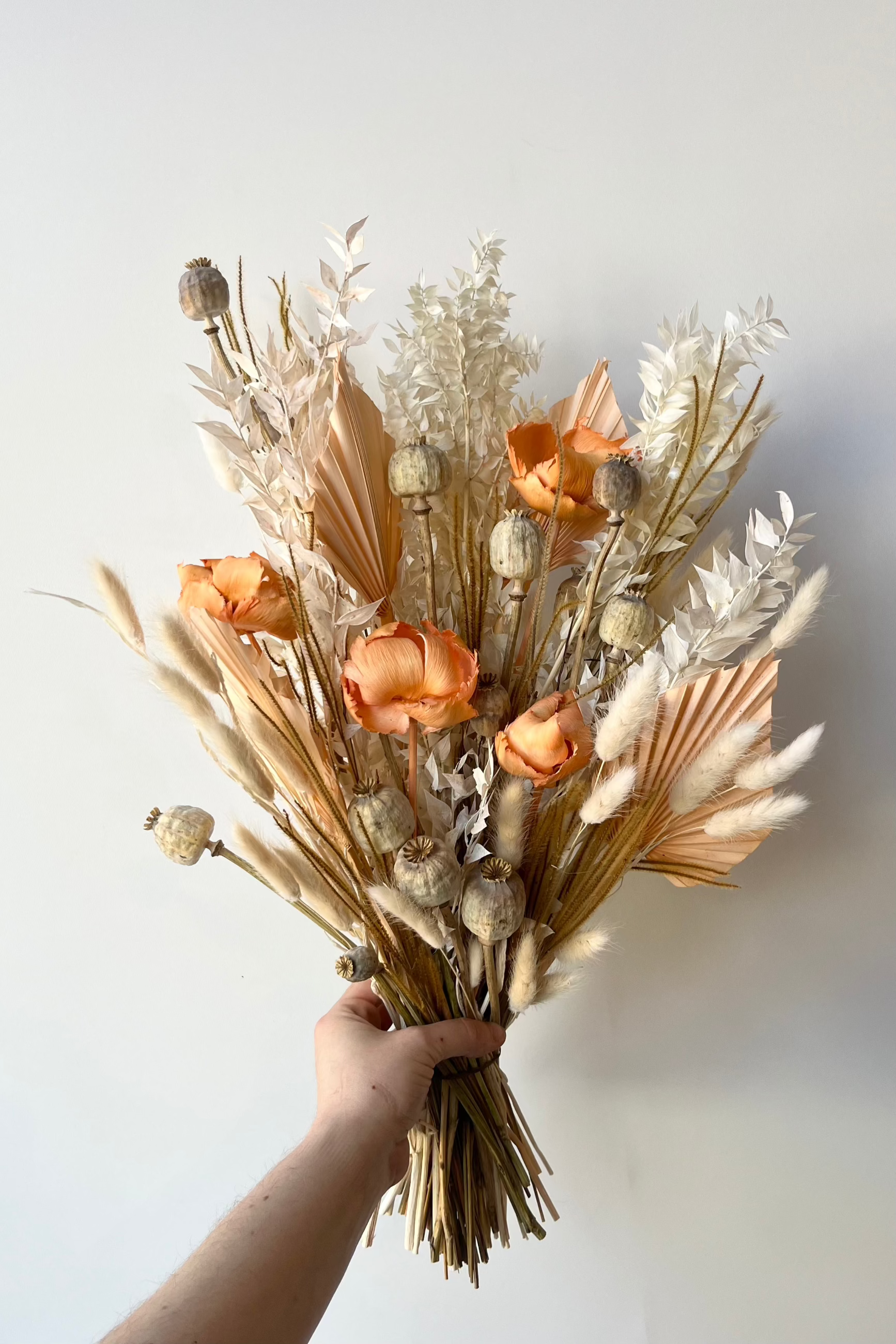 Creamsickle dried floral arrangement with shades of cream, white and peach designed by Sprout Home and being held in hand against a white wall. ©Sprout Home #size_$85