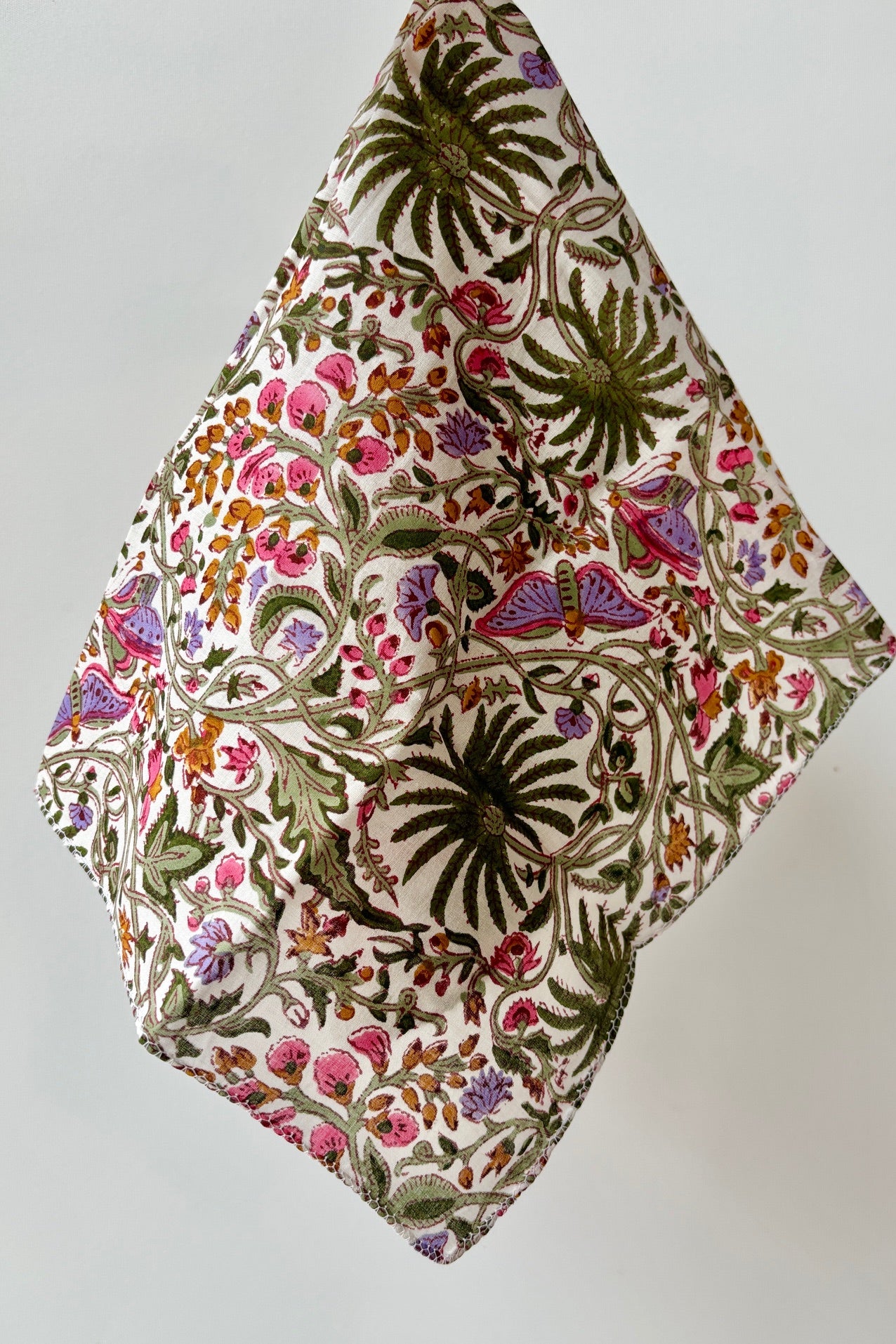 Hand sewn fabric napkin with green and pink floral butterfly and palm motif on a white background